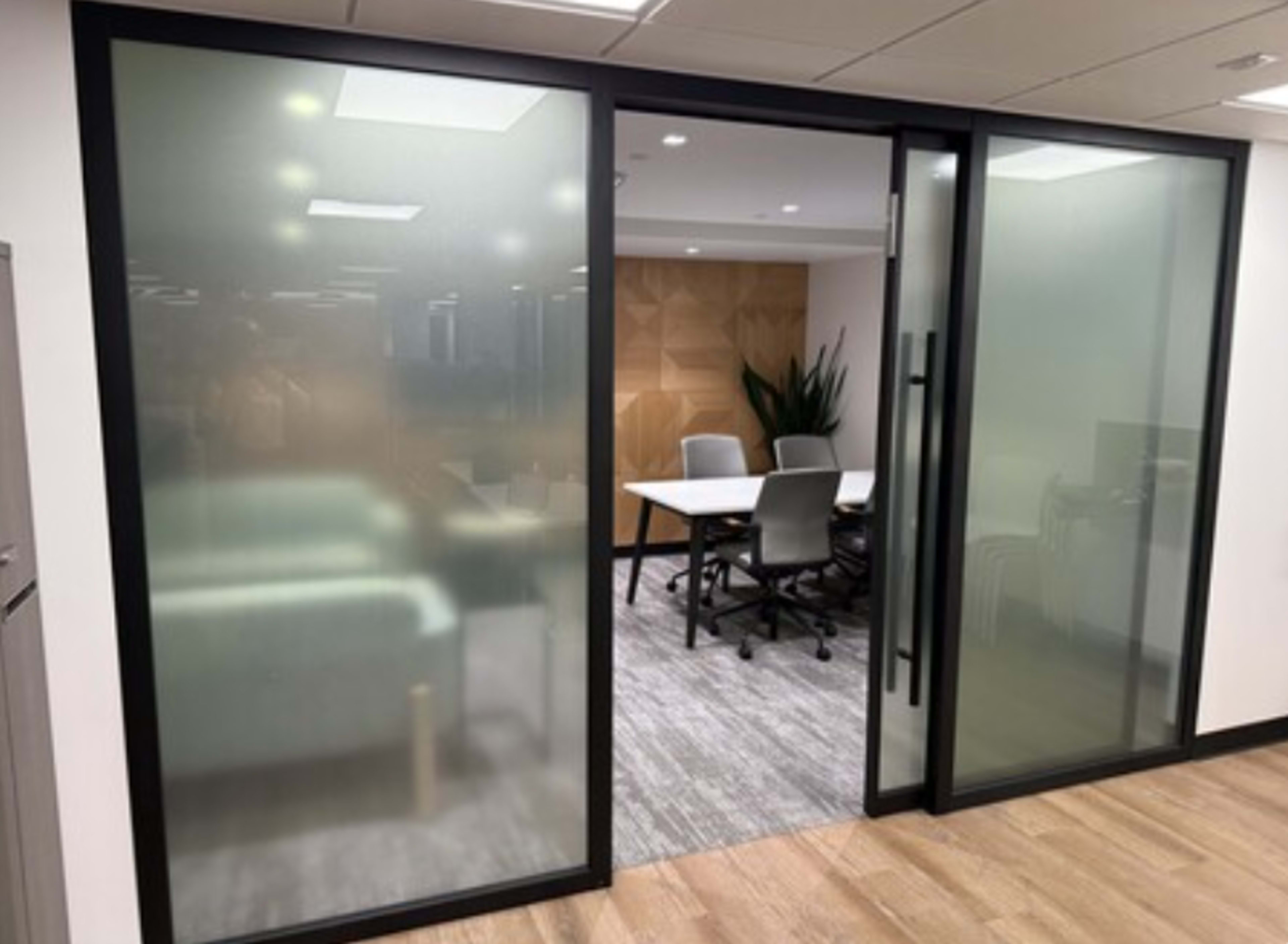 The image shows a conference room with frosted glass walls and a table surrounded by chairs, visible through the entrance.
