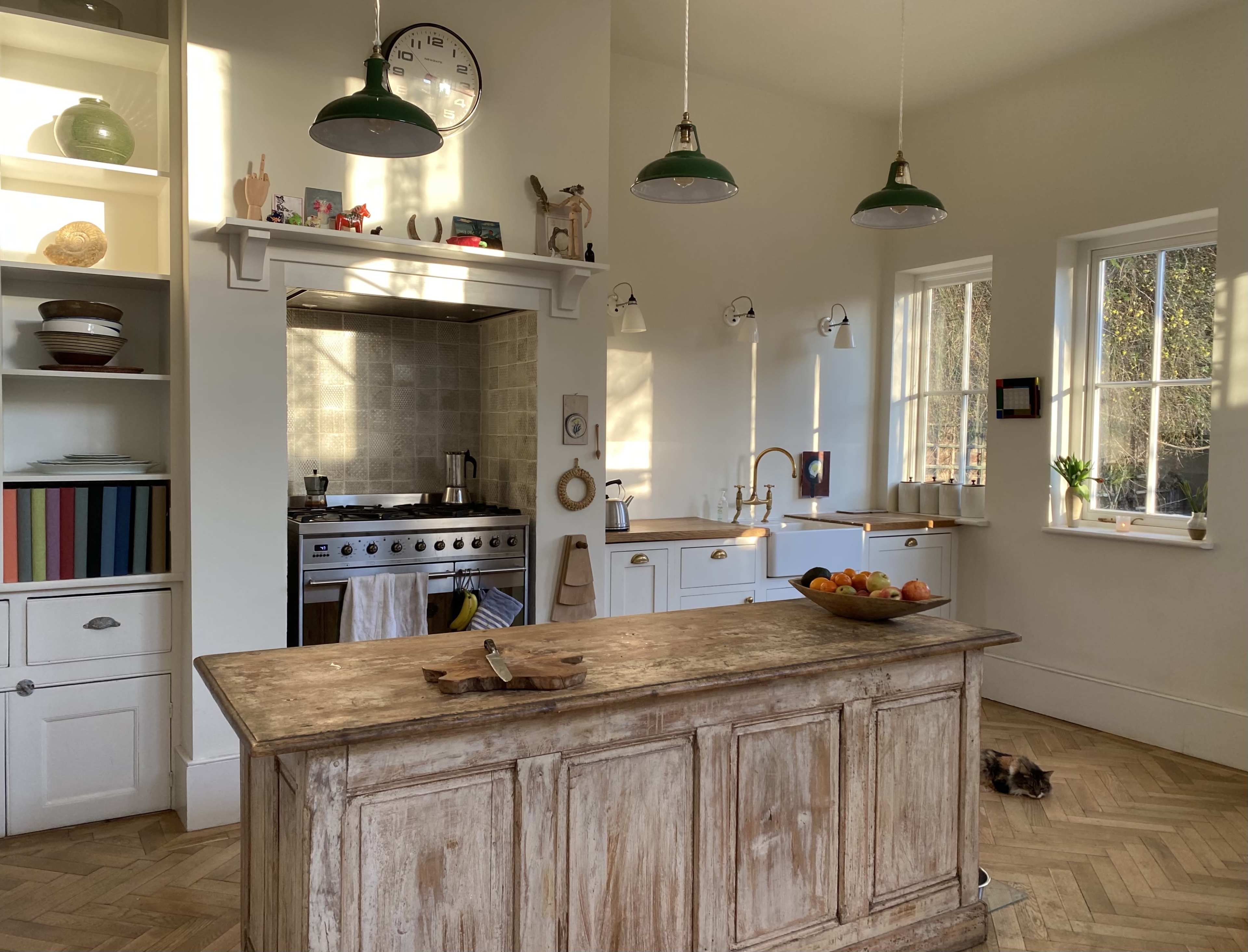 A spacious kitchen features a central wooden island, a stove with overhead lighting, and large windows allowing natural light to illuminate the space.