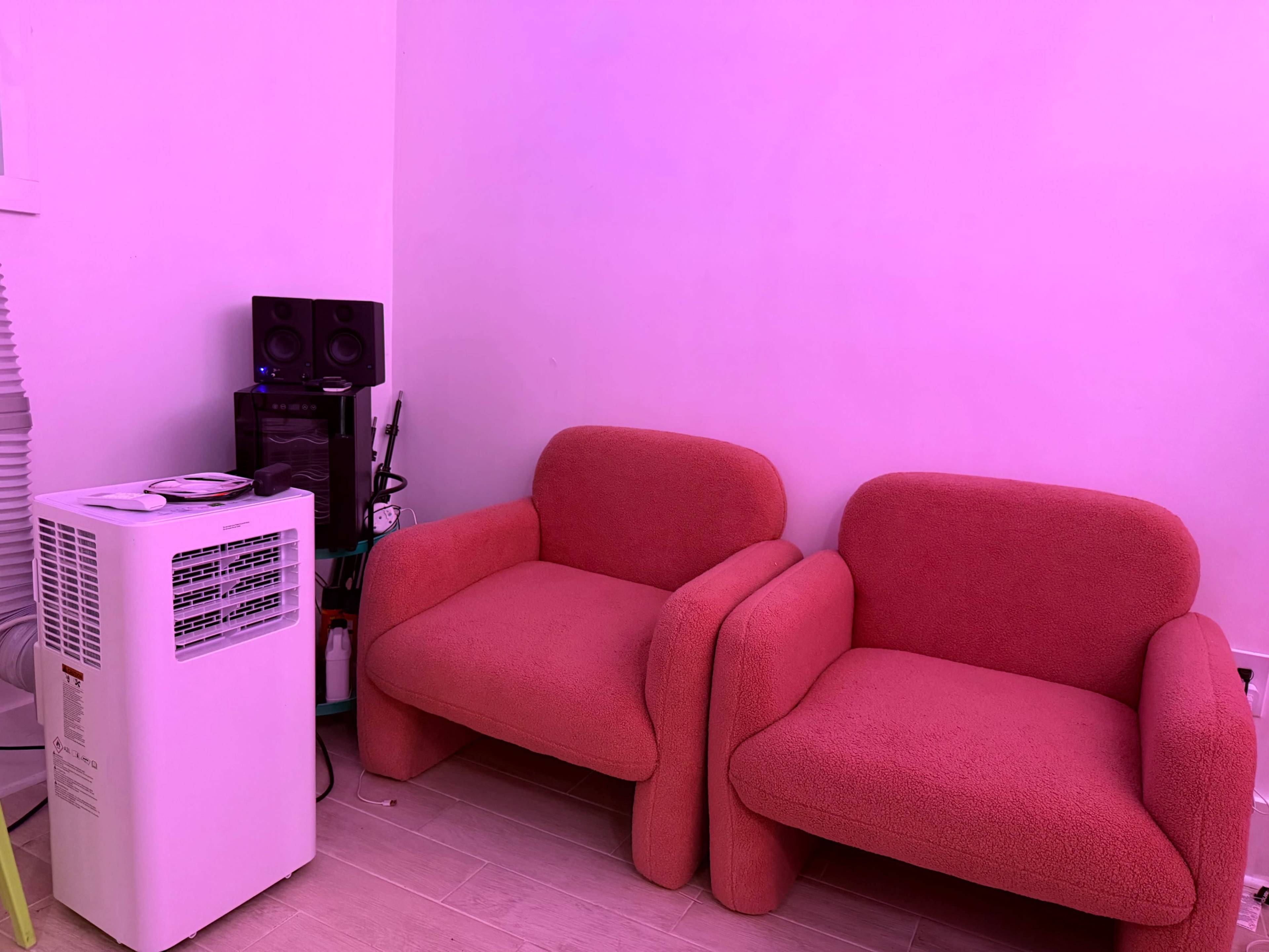 The image shows two pink chairs positioned next to a white air conditioning unit in a room with a pink hue.