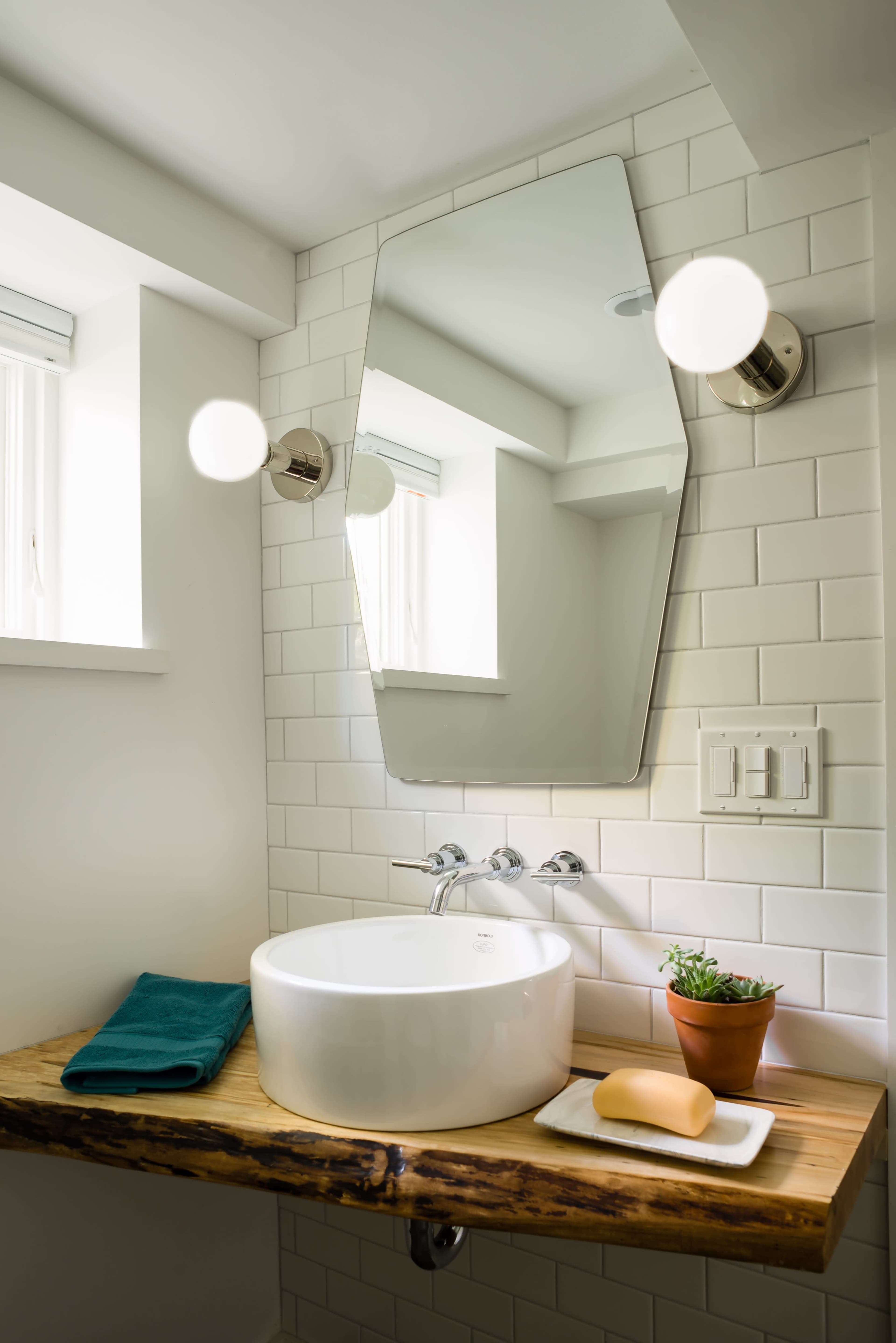A modern bathroom features a round vessel sink on a wooden countertop, complemented by a large mirror and light fixtures.