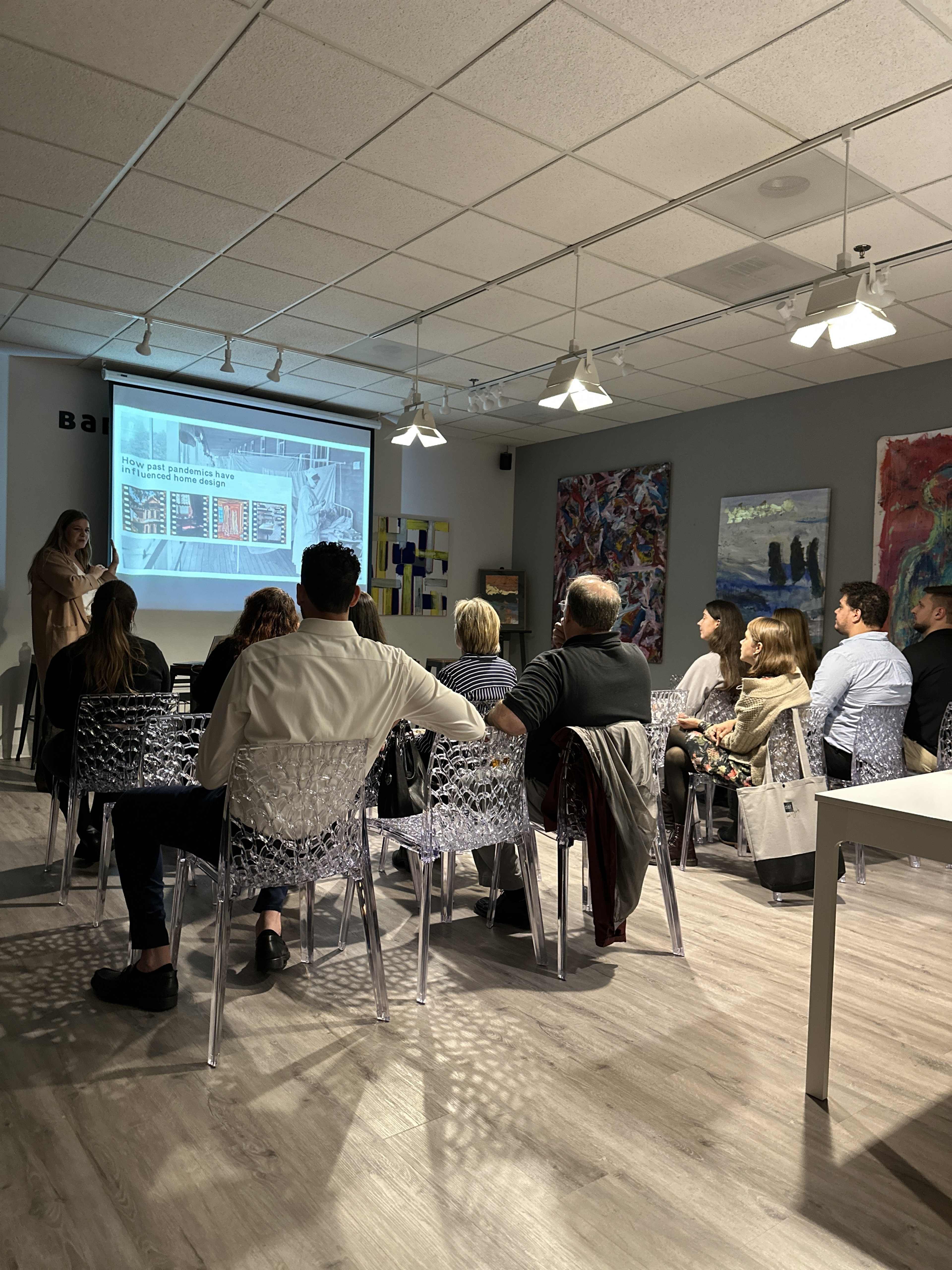 A group of people is seated in a room, watching a presentation displayed on a screen at the front.