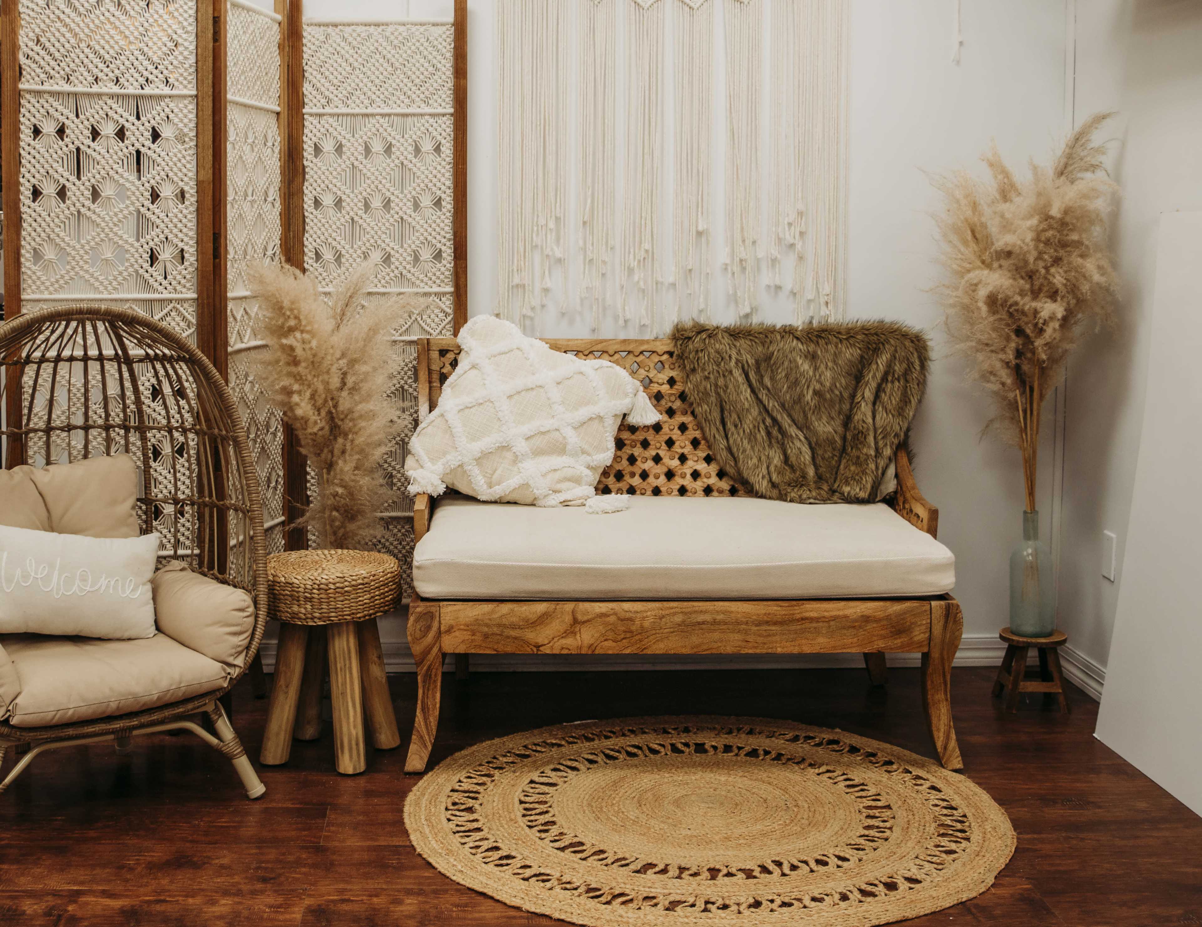 A cozy living space with a wooden couch adorned with decorative pillows, a woven rug on the floor, and potted pampas grass beside a wicker chair.
