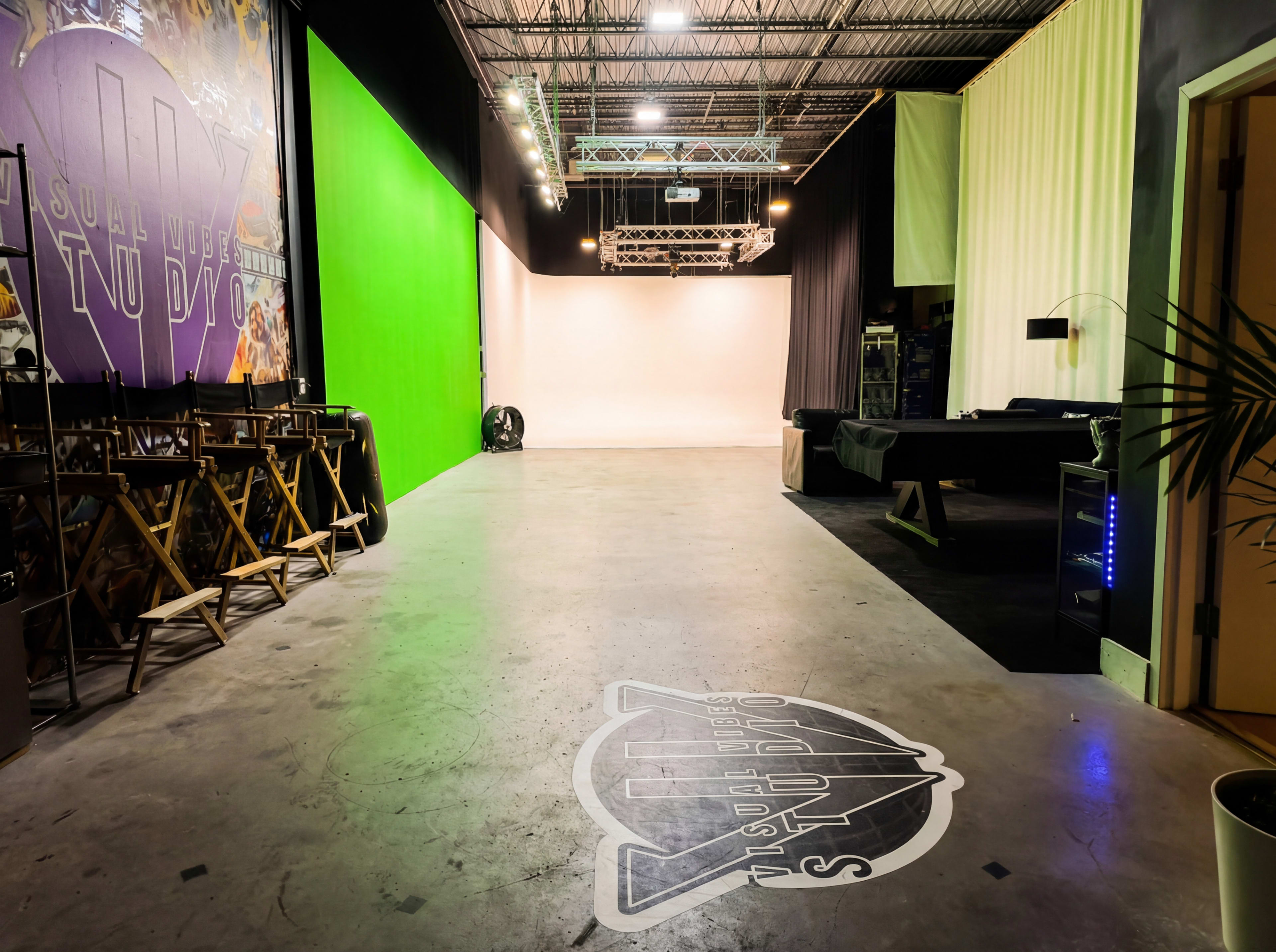 The image shows a spacious studio interior featuring green and white backdrops, director's chairs, and a logo on the floor.