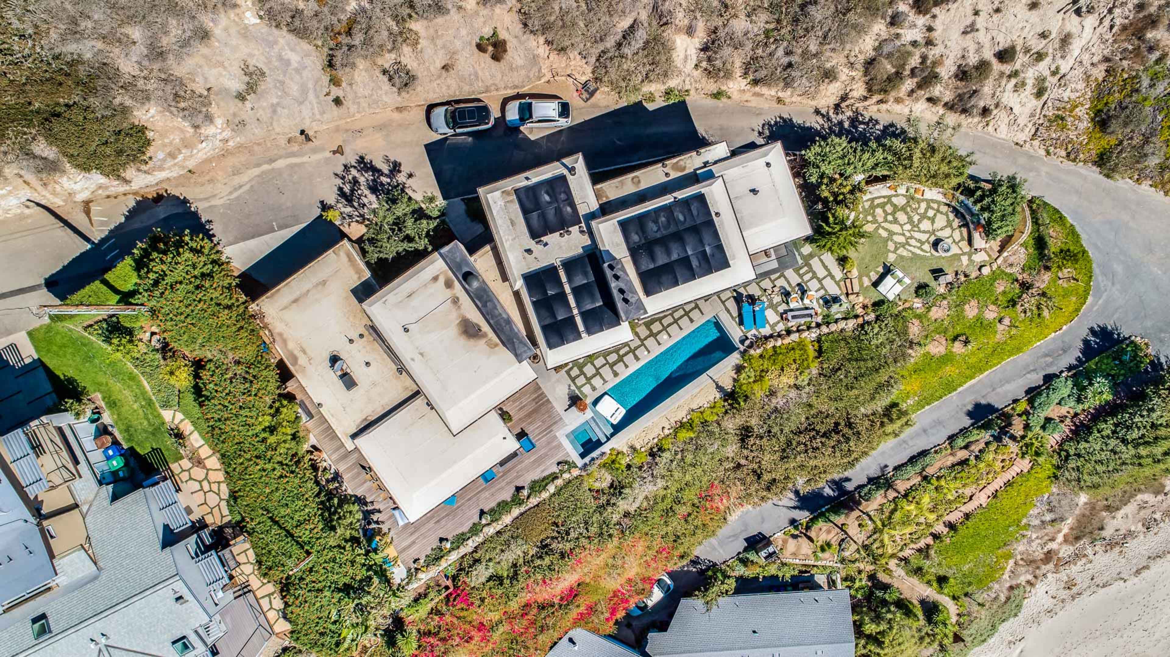 The image shows an aerial view of a residential property featuring multiple buildings, a swimming pool, and landscaped gardens along a winding road.