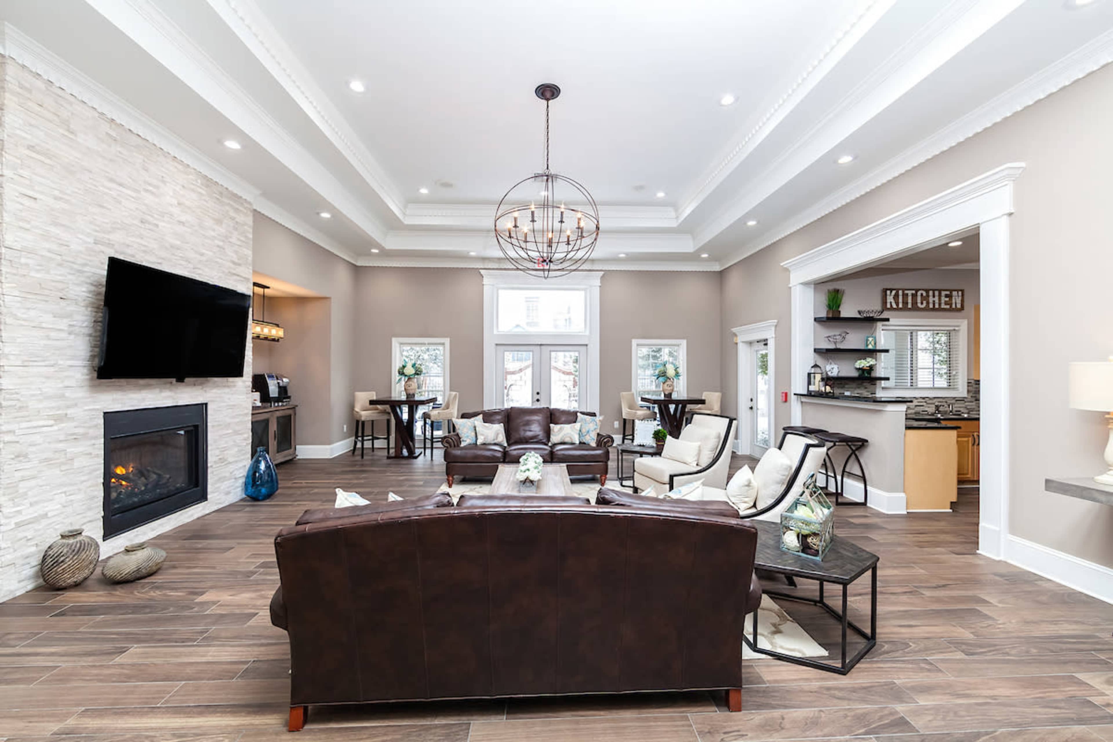 The spacious living area features a leather sofa, a stone fireplace, and a large television, with modern furnishings and an open kitchen visible in the background.