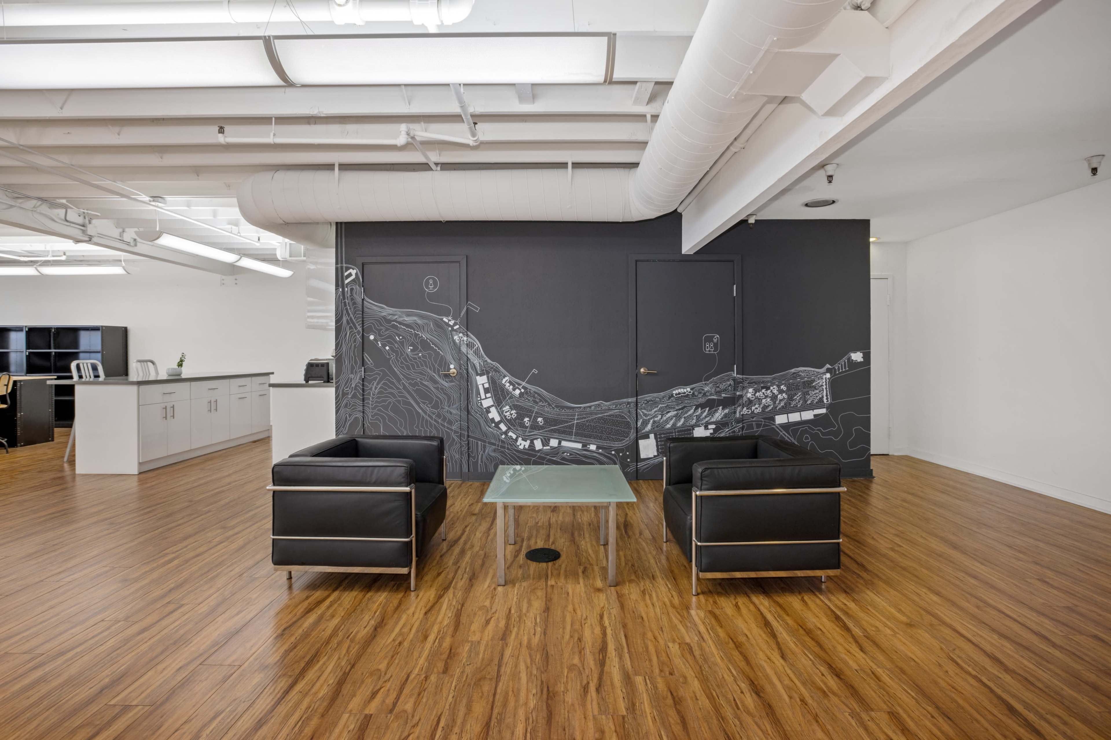 A modern office space with two black chairs facing a glass table in front of a wall featuring a graphic map design.