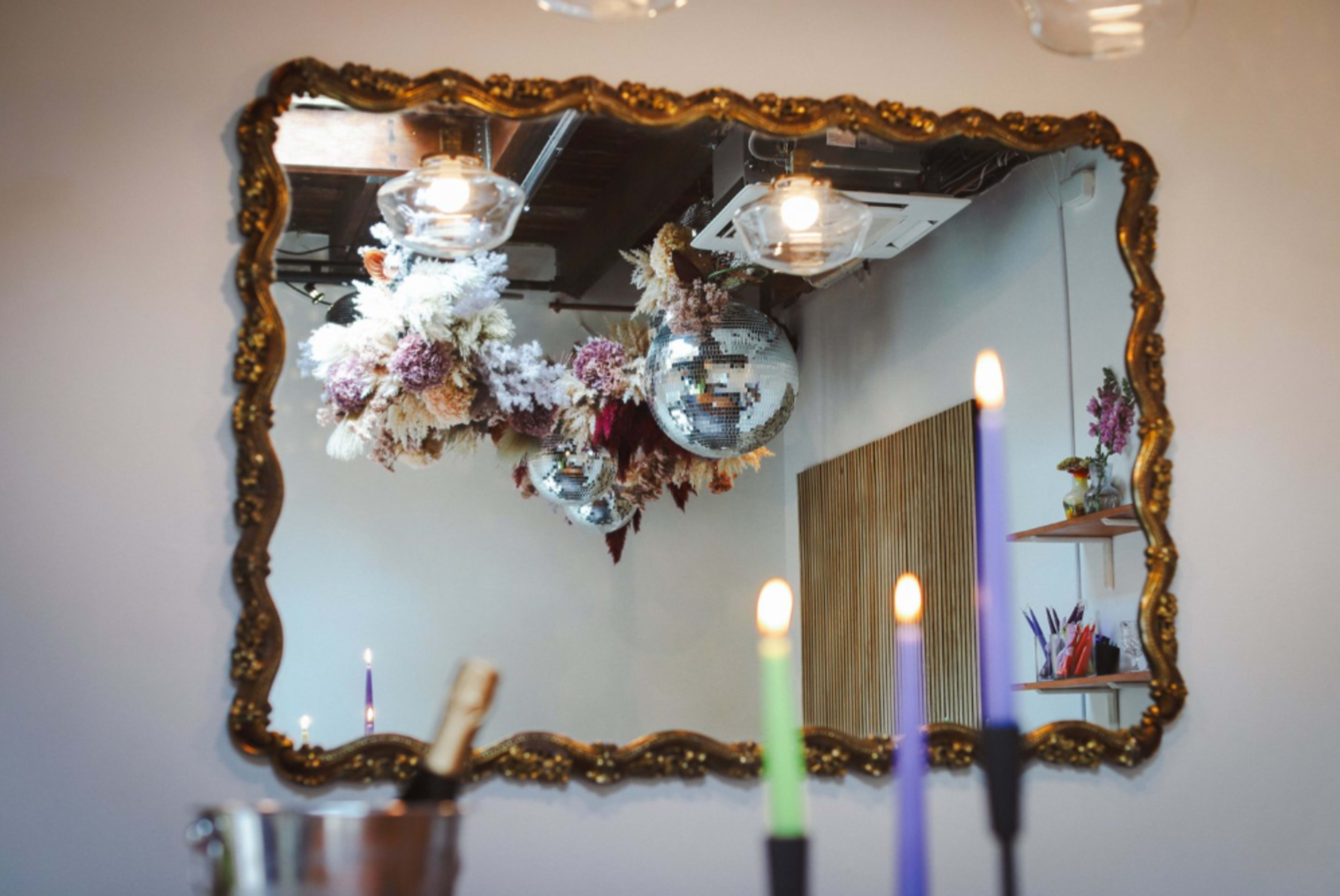 A decorative mirror reflects disco balls and floral arrangements hanging from the ceiling, while lit candles in various colors are arranged in the foreground.