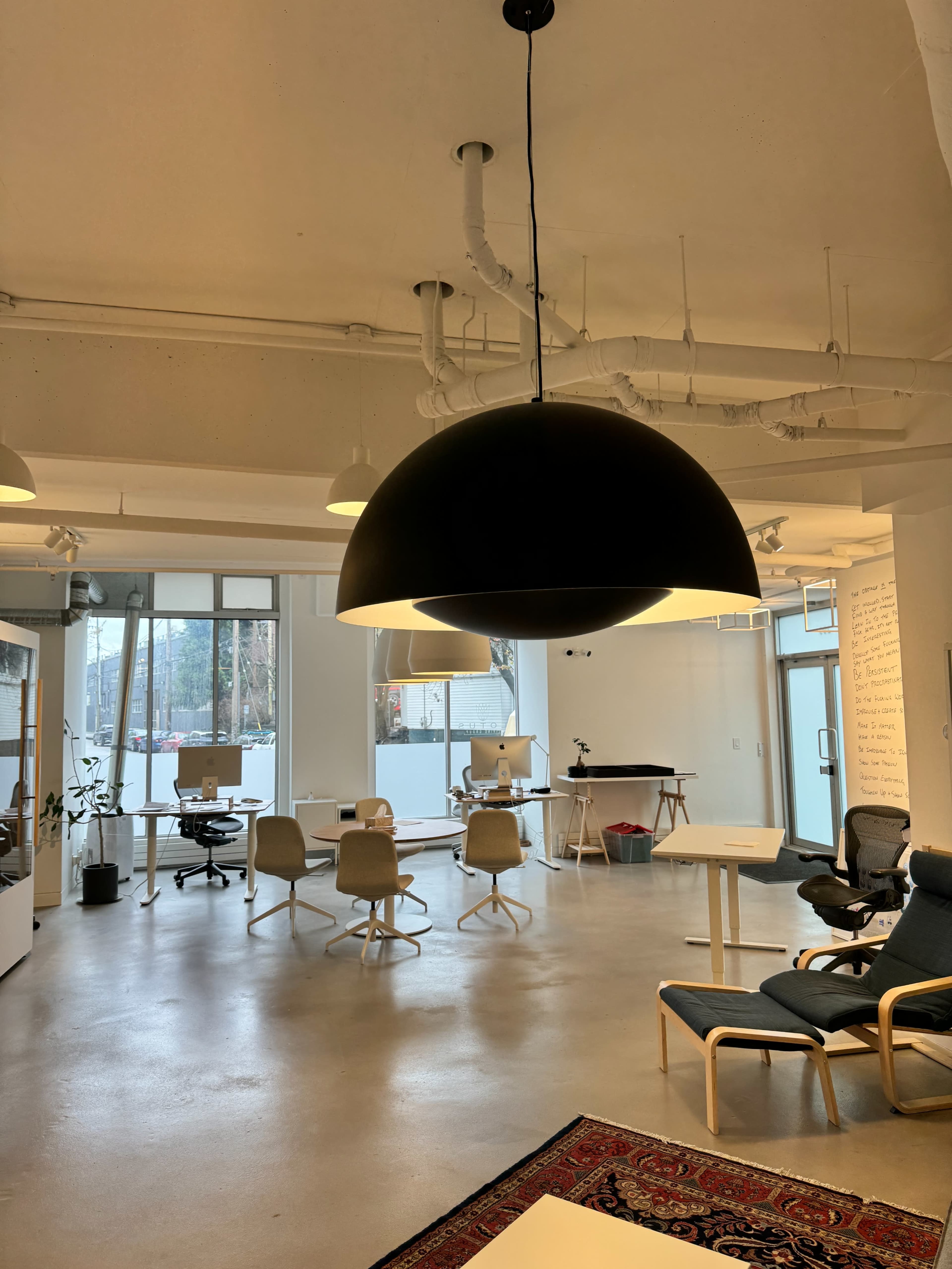 A modern office space featuring a large black pendant light, several workstations, and a mix of chairs around a table.