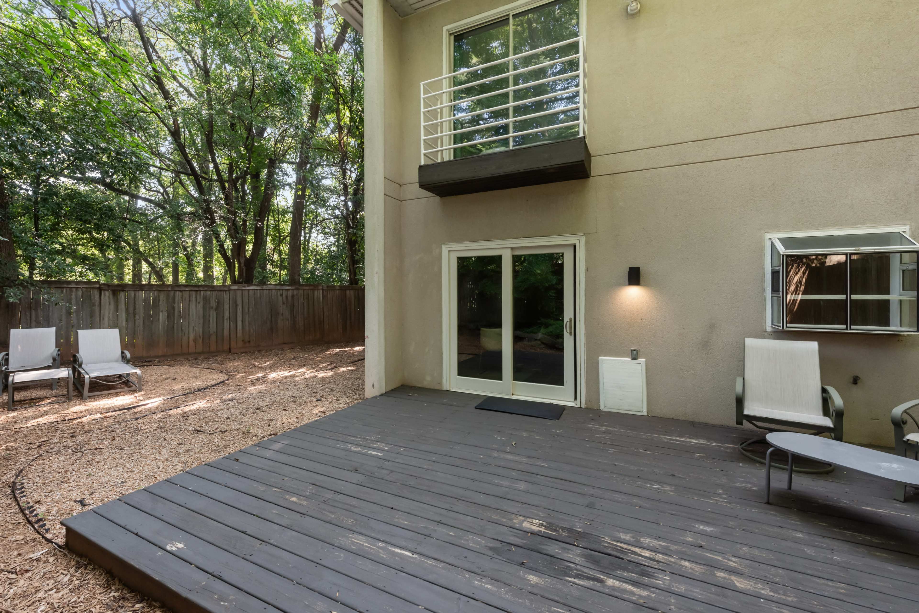 The image shows a wooden deck outside a building, surrounded by trees and featuring a seating area with lounge chairs.