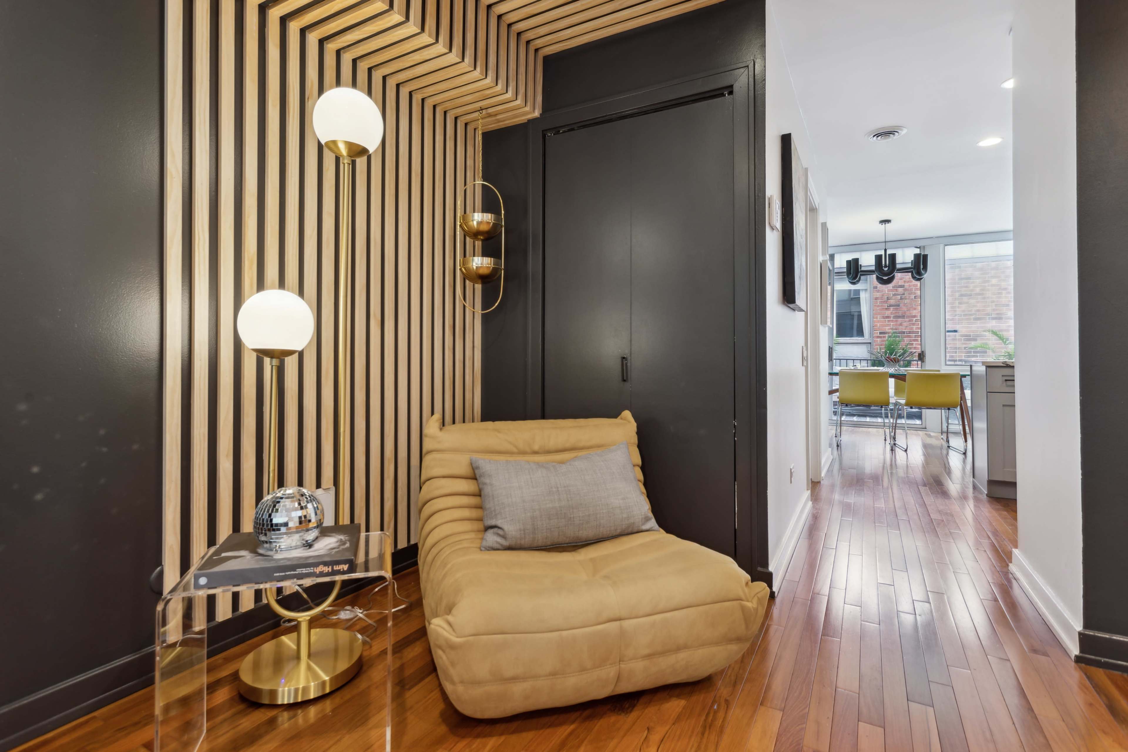 A modern hallway featuring a wooden slat accent wall, a plush chair, and a glass side table with a decorative item.