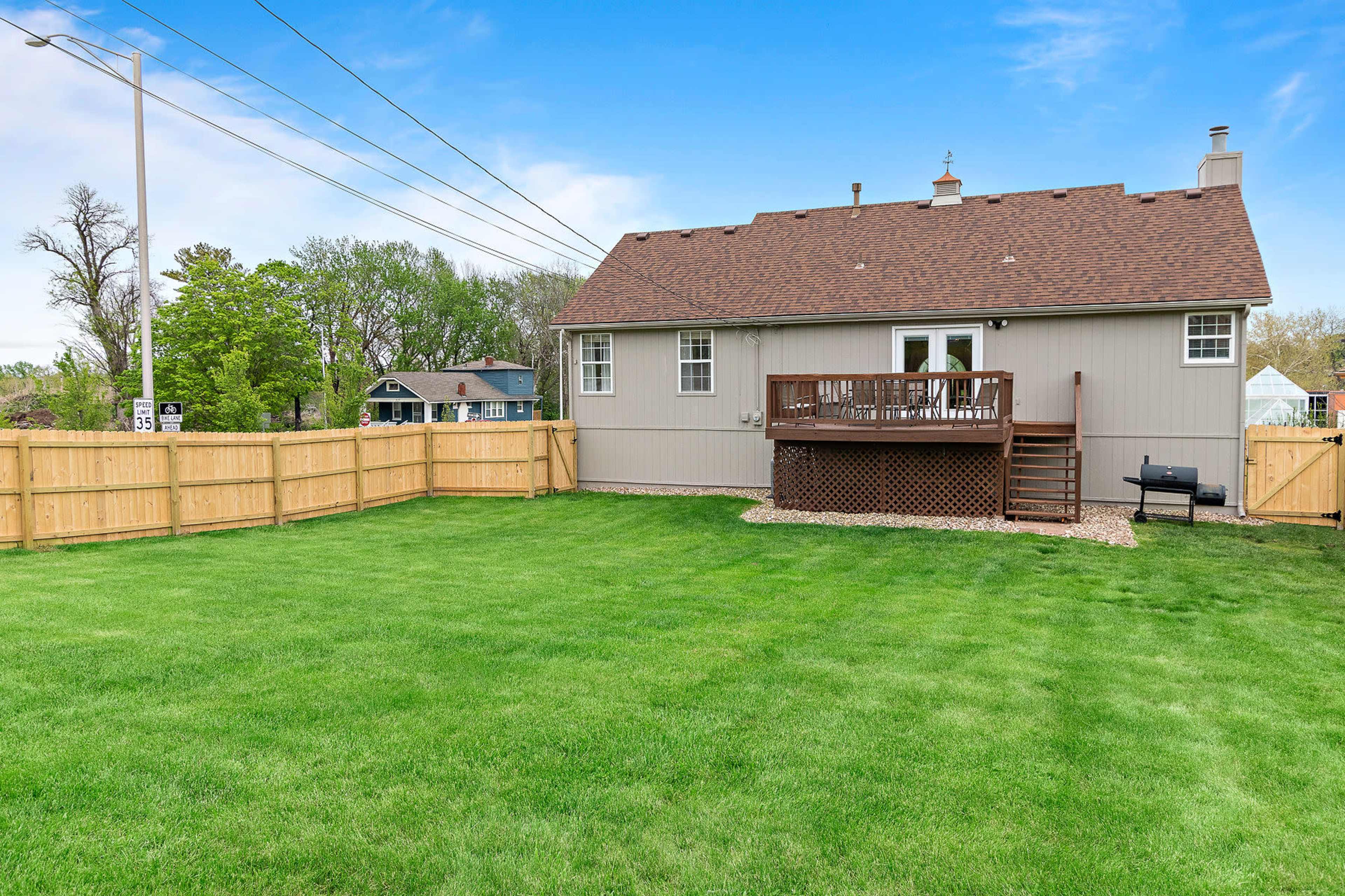 A fenced backyard with a well-manicured lawn and a two-story house featuring a deck and a barbecue grill.