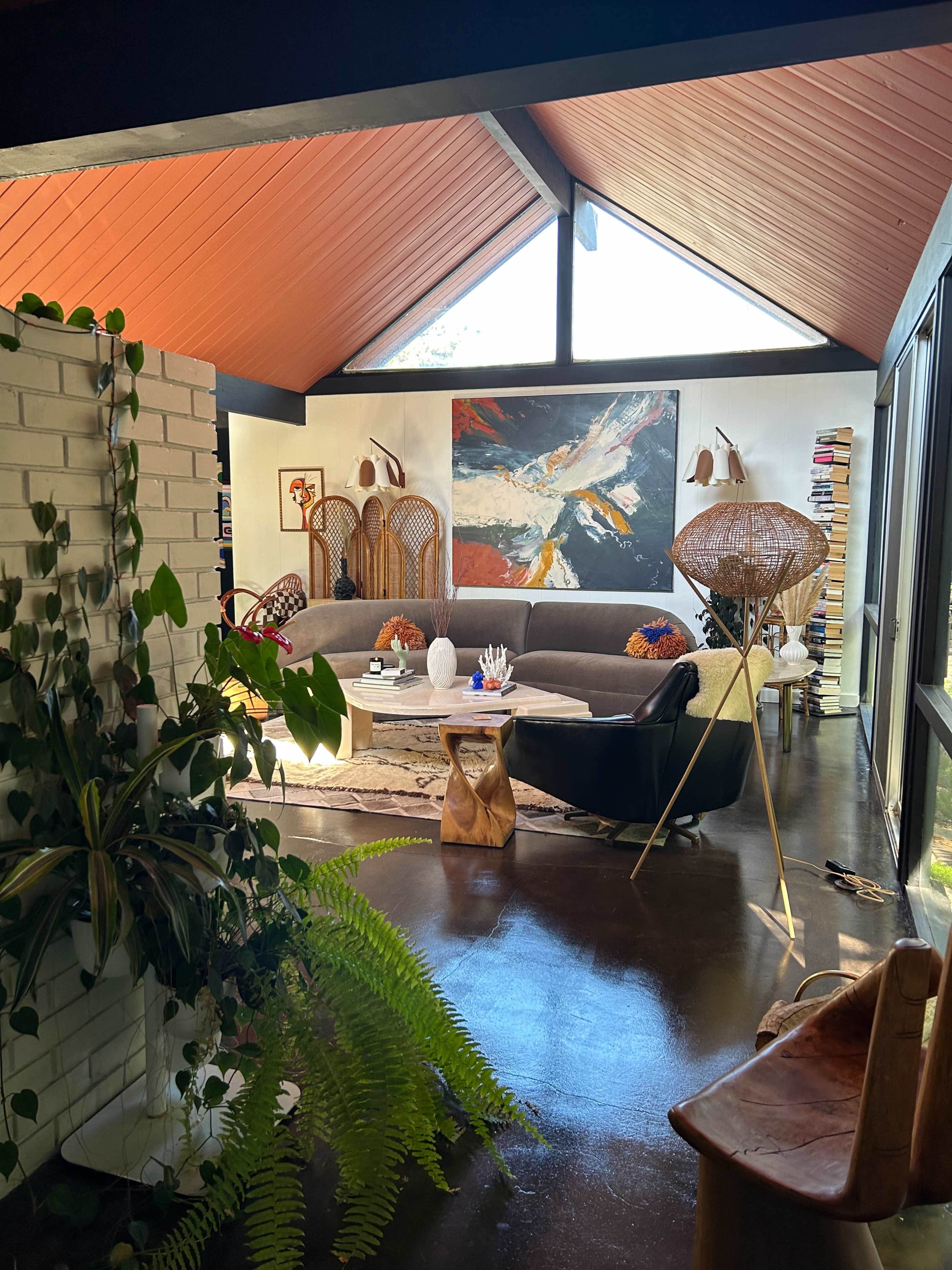 A modern living room with a high ceiling, large windows, a mix of furniture styles, and a prominent piece of contemporary art on the wall.