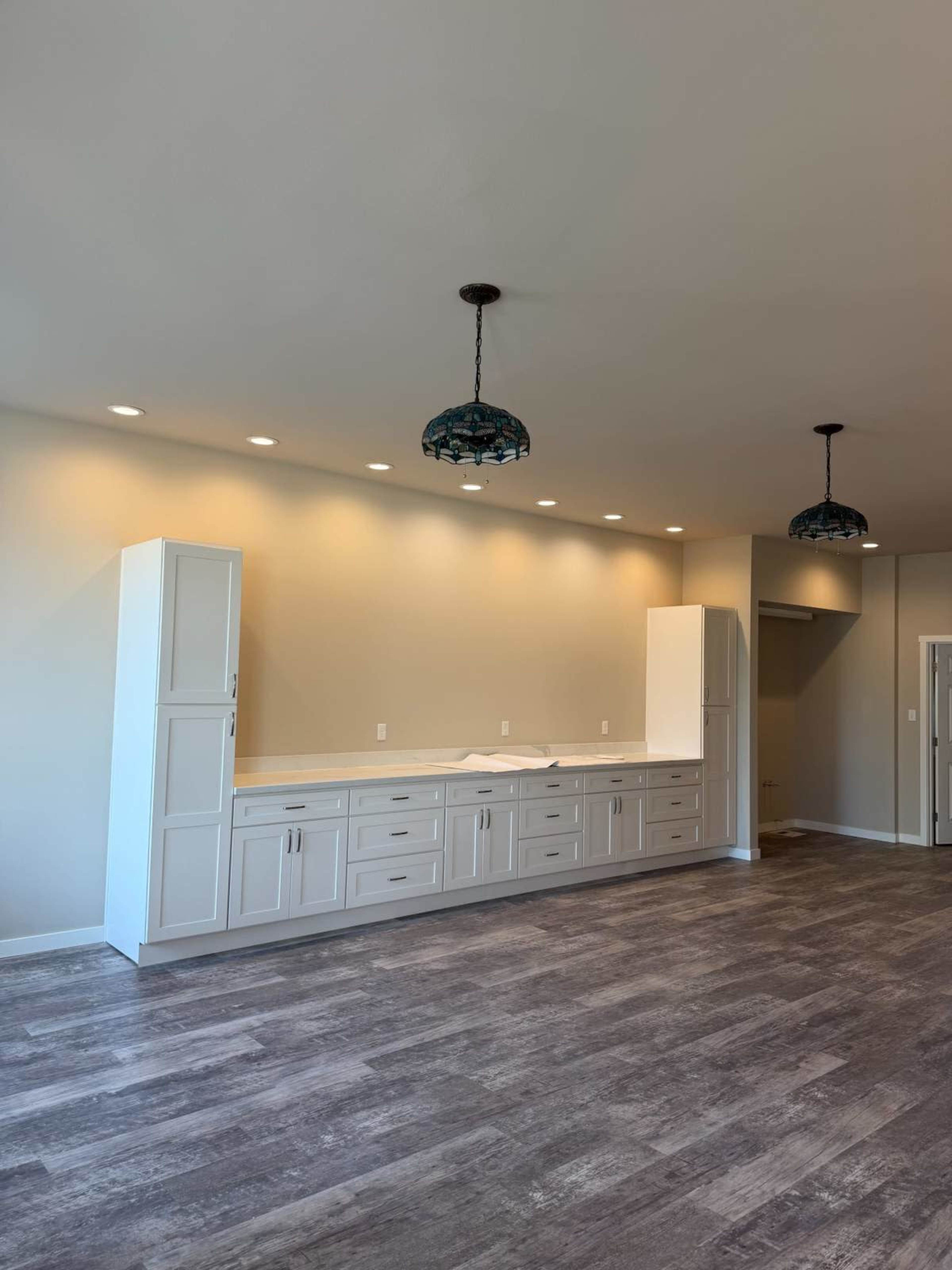The image shows a spacious kitchen area with light-colored cabinetry, two pendant lights, and a wooden floor.