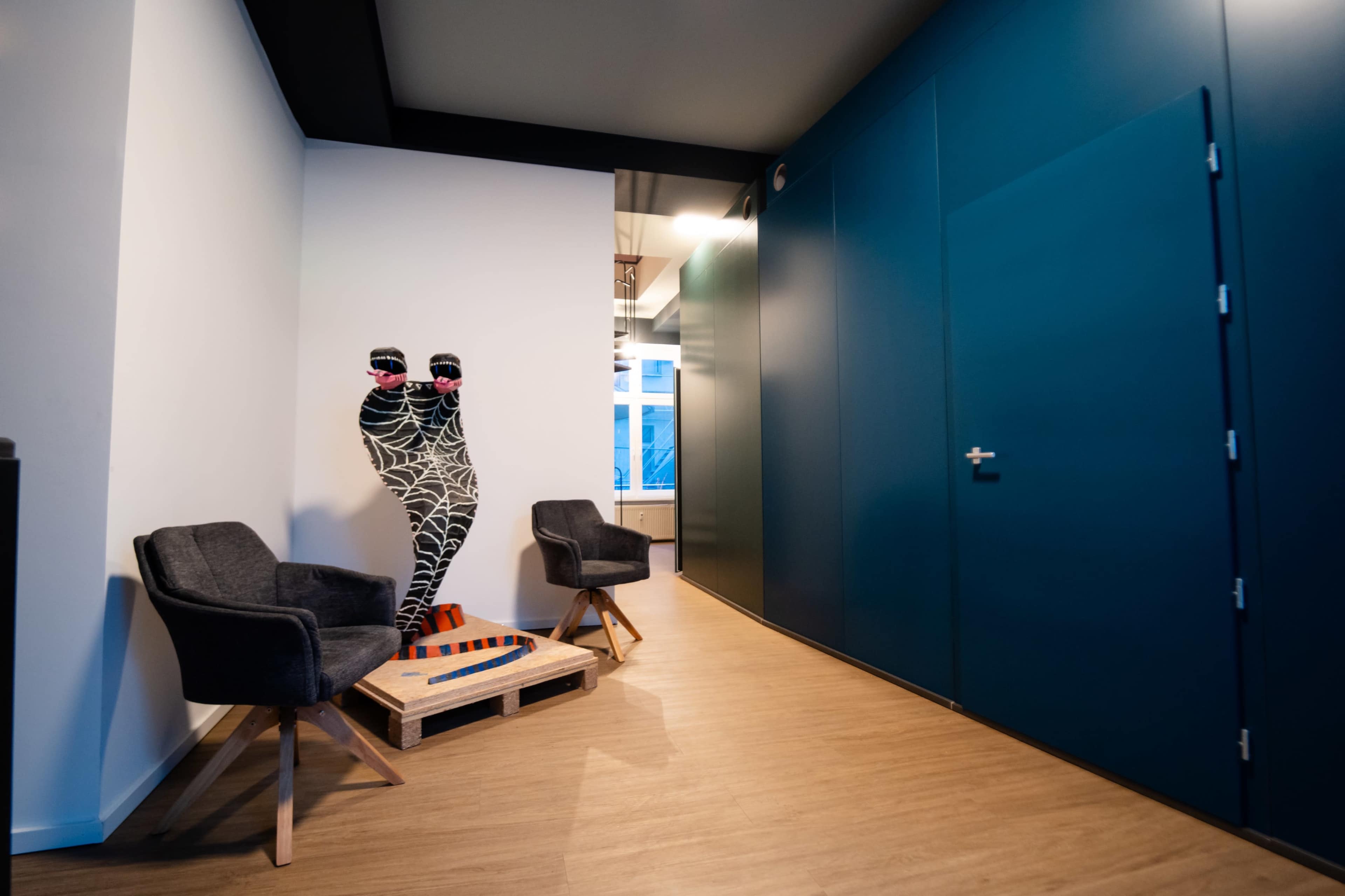 The image shows a hallway interior featuring two chairs and a decorative figure with a web-like design.