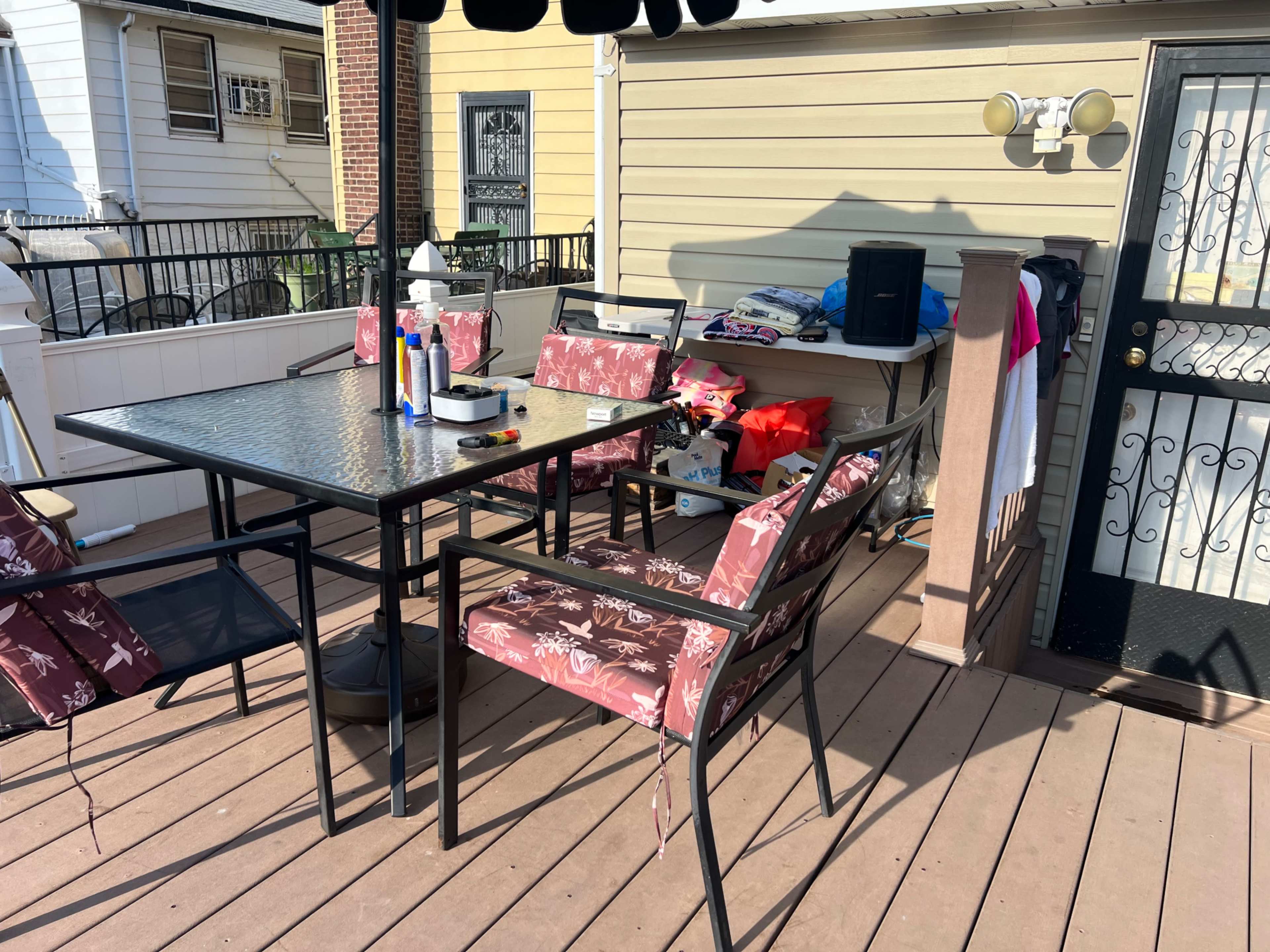 The image shows a patio area with a glass-top dining table surrounded by four chairs, a small speaker, and various items on a nearby table.