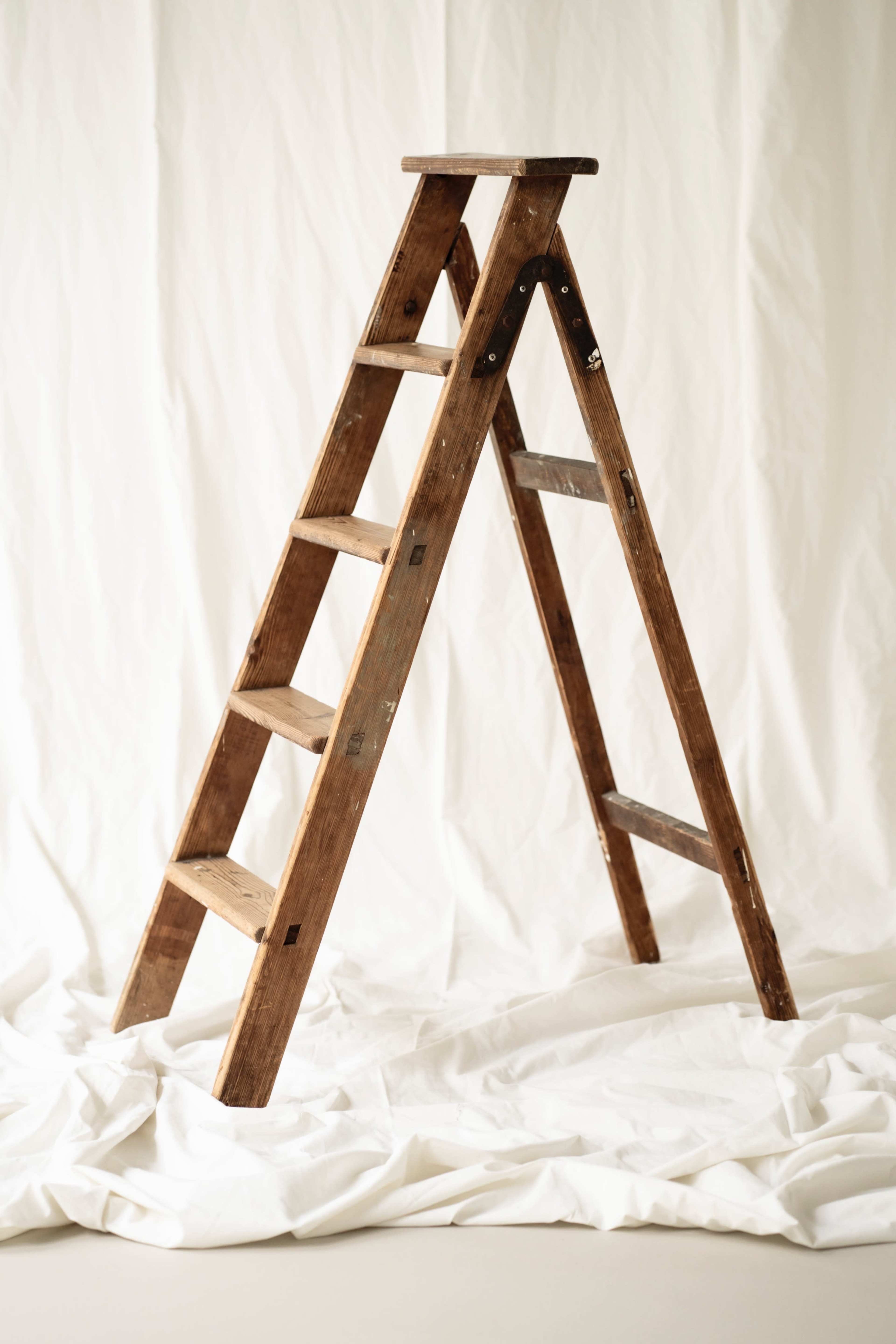 A wooden step ladder stands against a white backdrop.