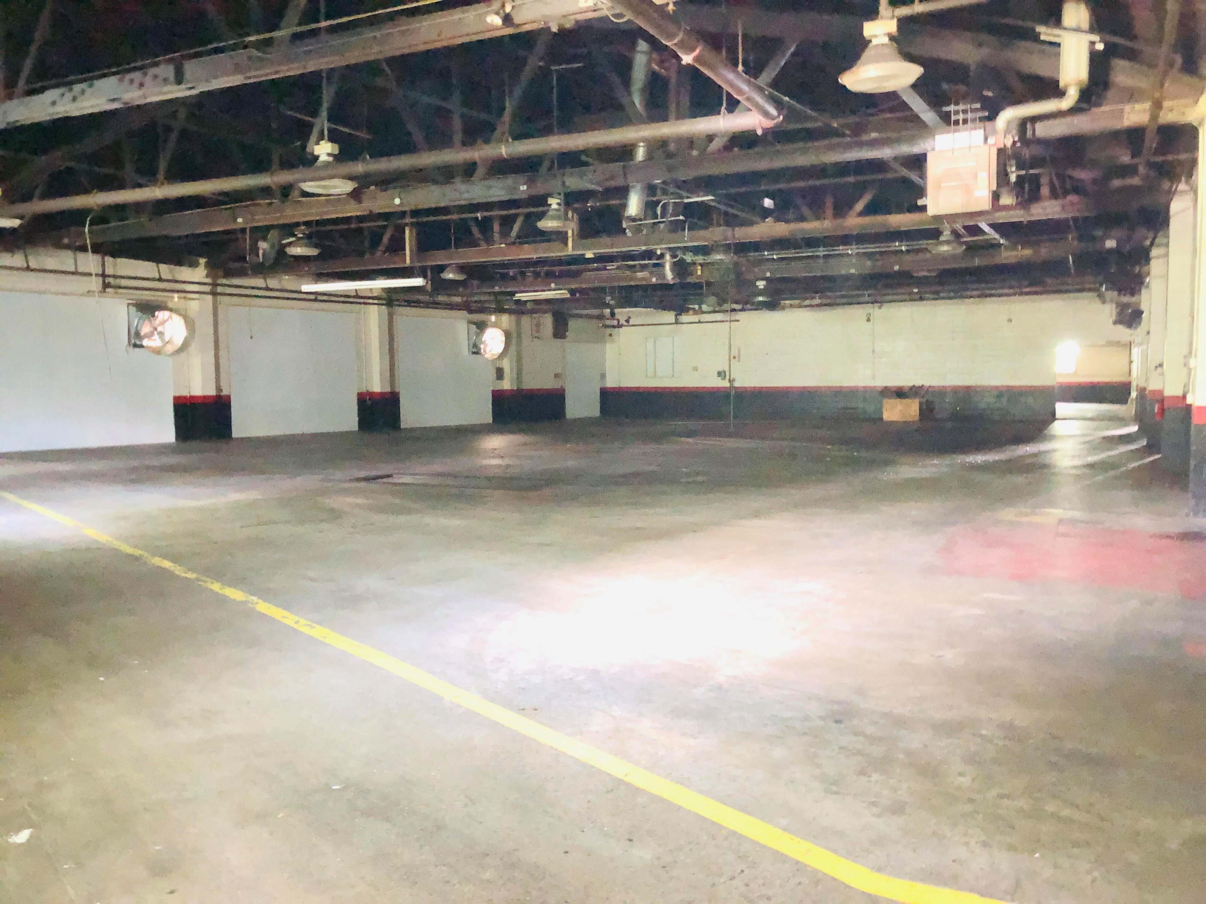 An empty industrial warehouse with high ceilings, exposed beams, and concrete floors.