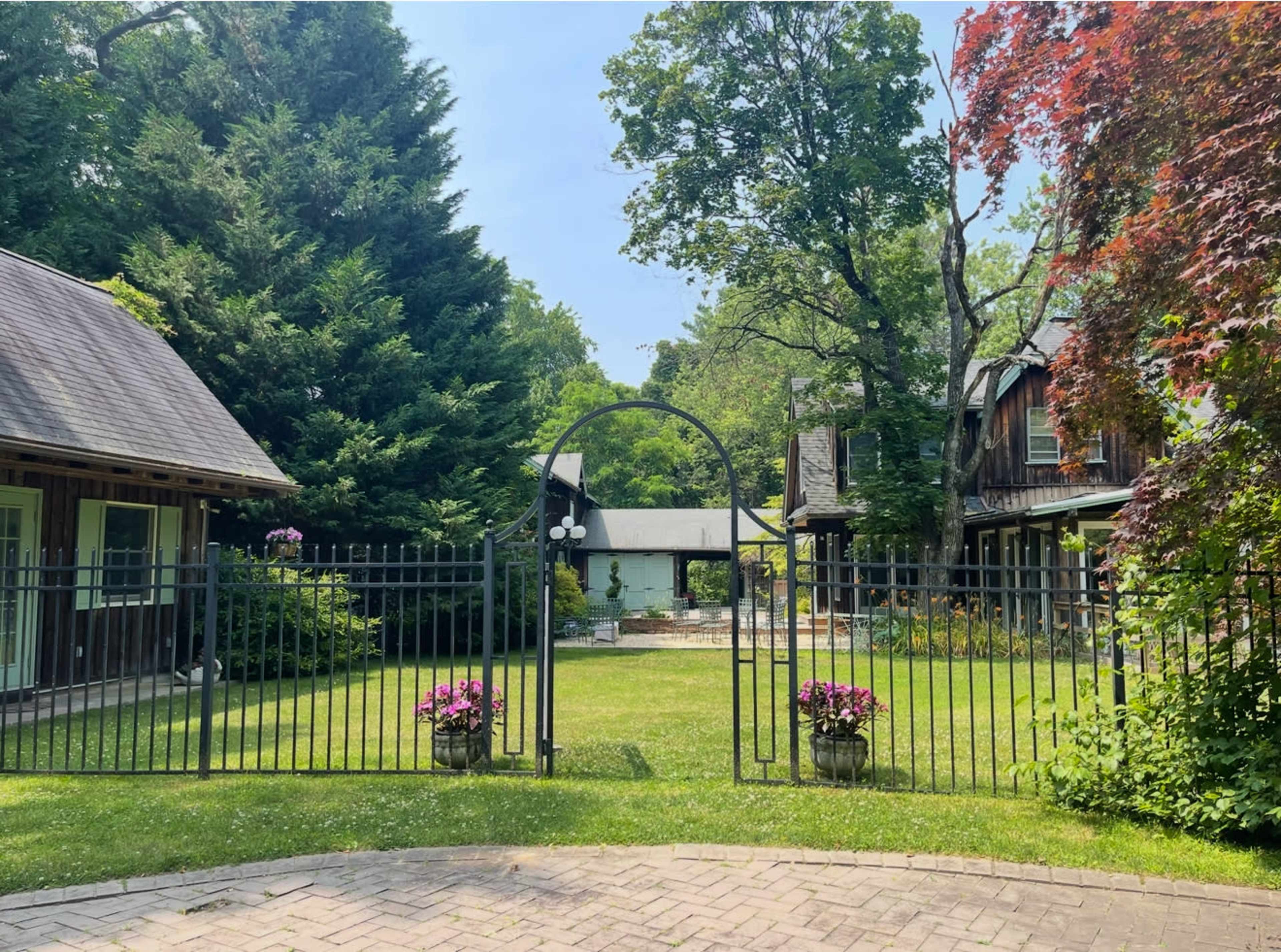 A wrought-iron gate opens to a landscaped courtyard surrounded by greenery and buildings.