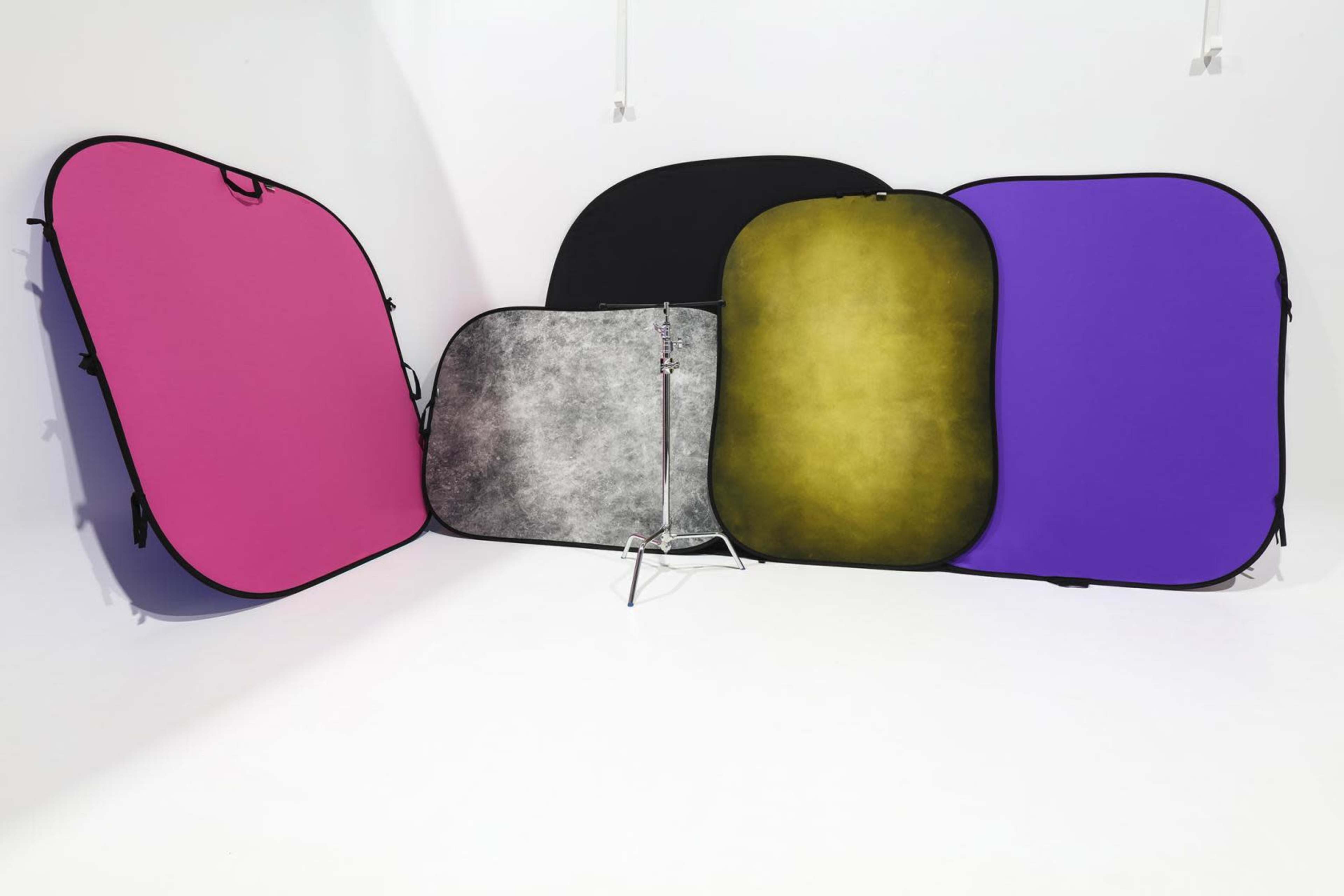 A collection of five colorful backdrop panels arranged next to a metal stand in a white studio setting.