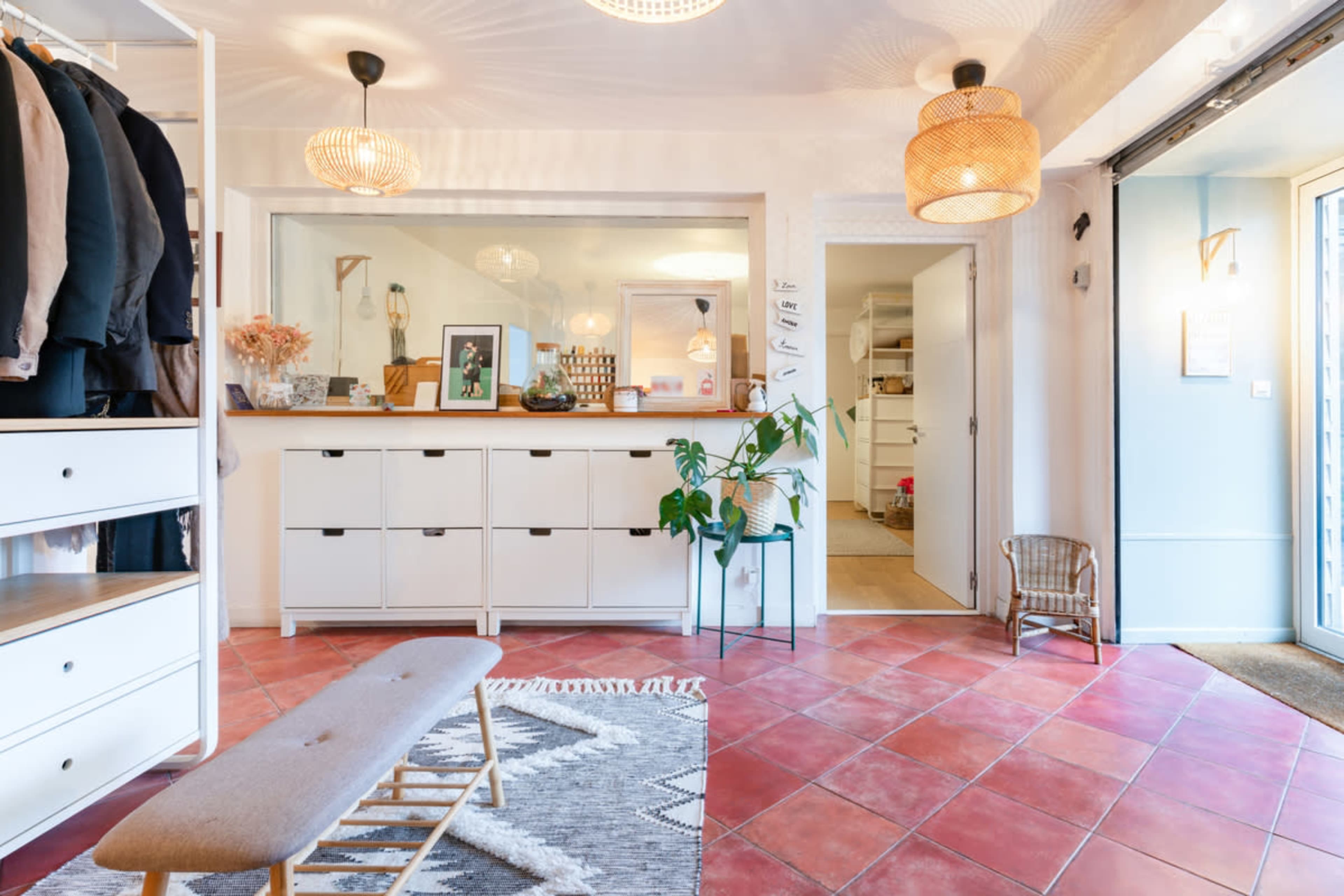 A spacious entryway features a coat rack, a low bench, and storage units against a wall, with decorative light fixtures overhead.