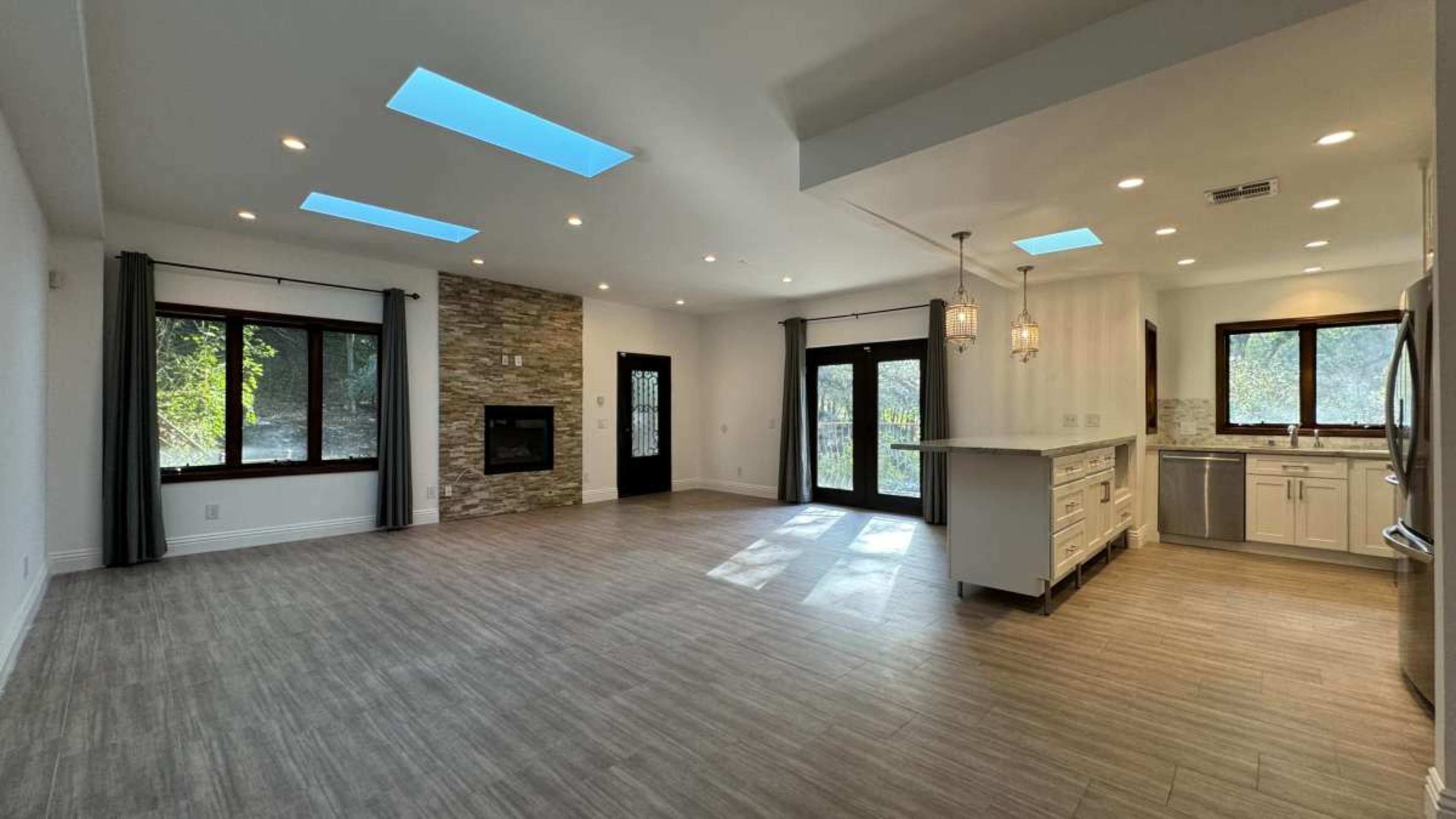 The spacious living area features a stone fireplace, large windows, and a modern kitchen with sleek cabinetry.