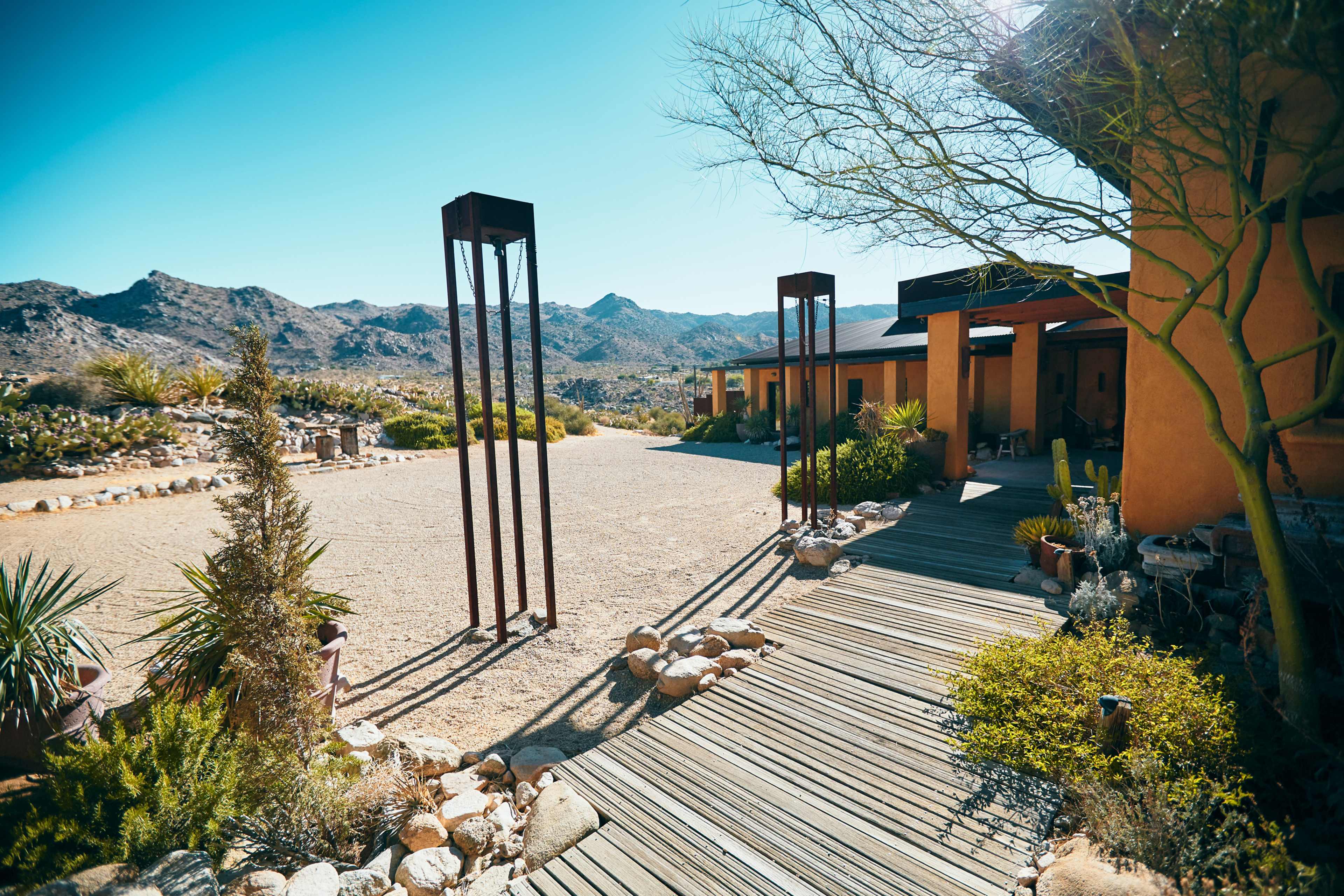 A pathway leading to a modern building surrounded by desert landscaping and rocky mountains in the background.