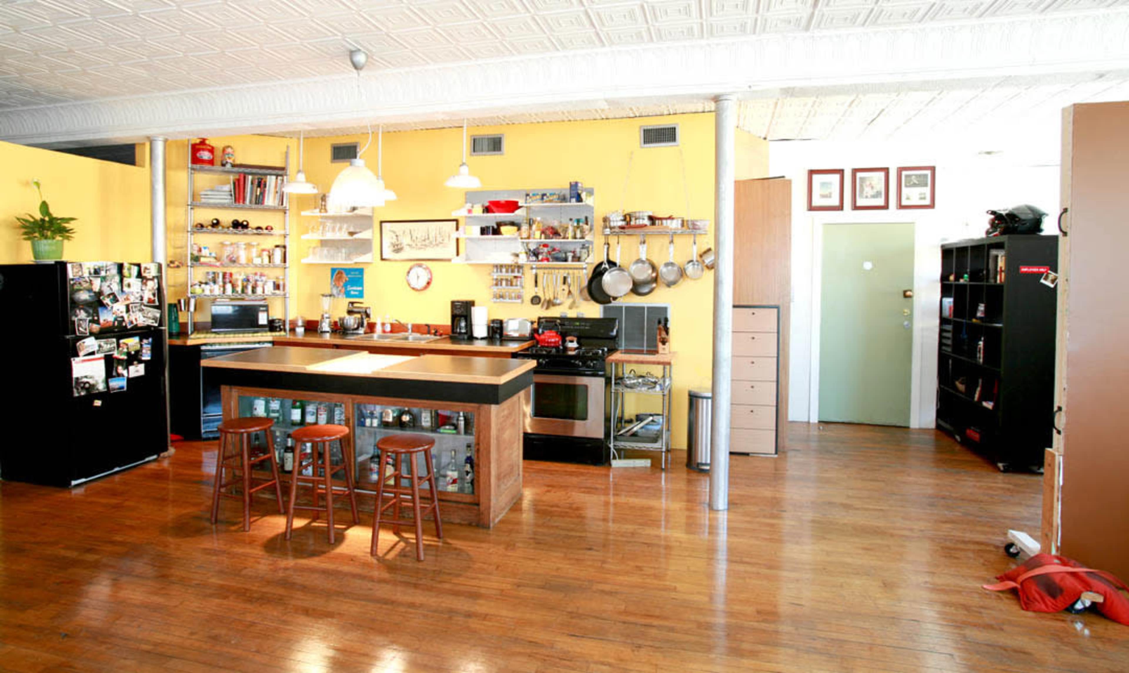 A spacious kitchen with a central island, wooden floors, and yellow walls, featuring shelves of kitchenware and appliances.