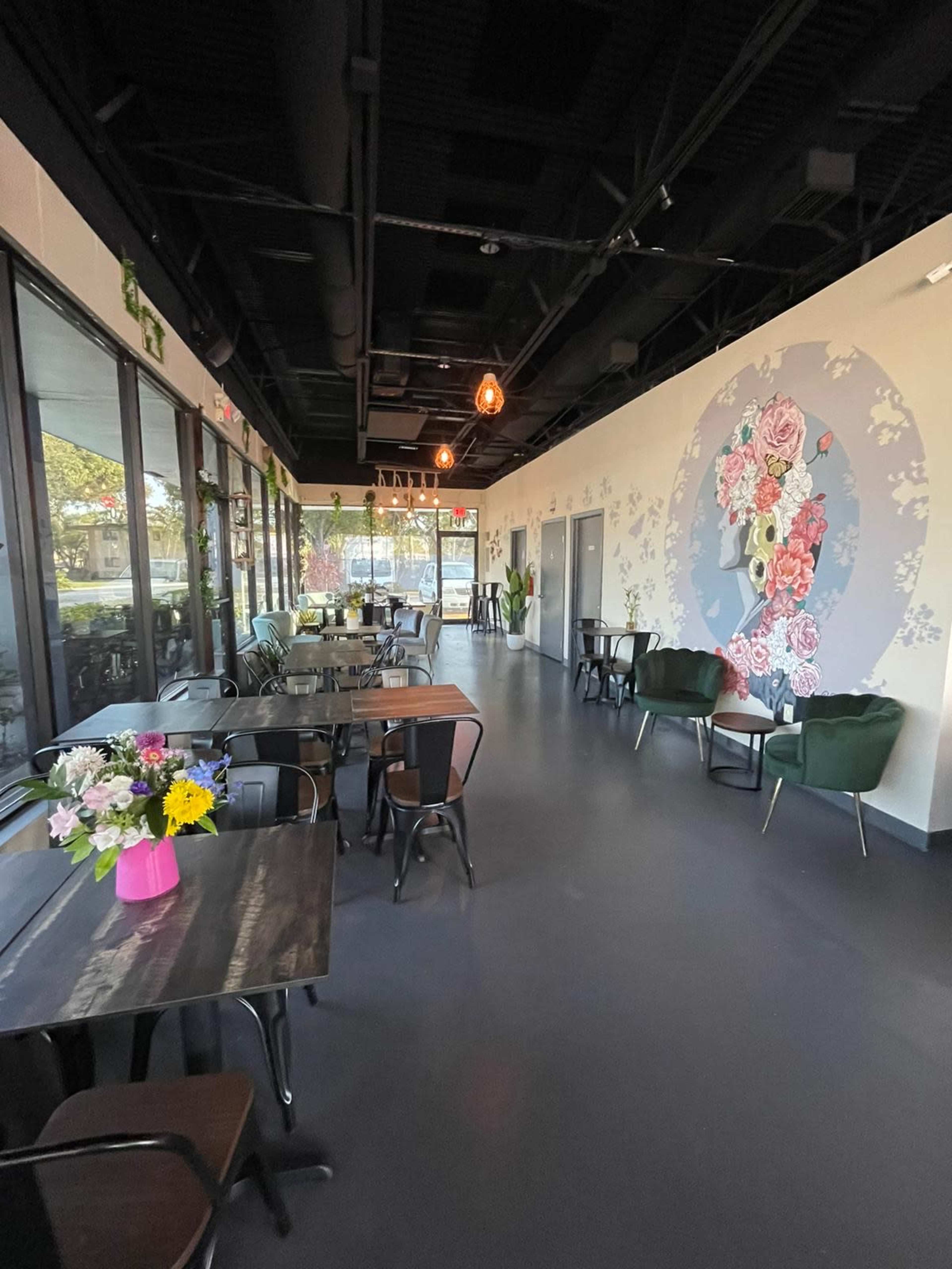 The interior of a modern café featuring tables, chairs, and a mural with floral designs on one wall.