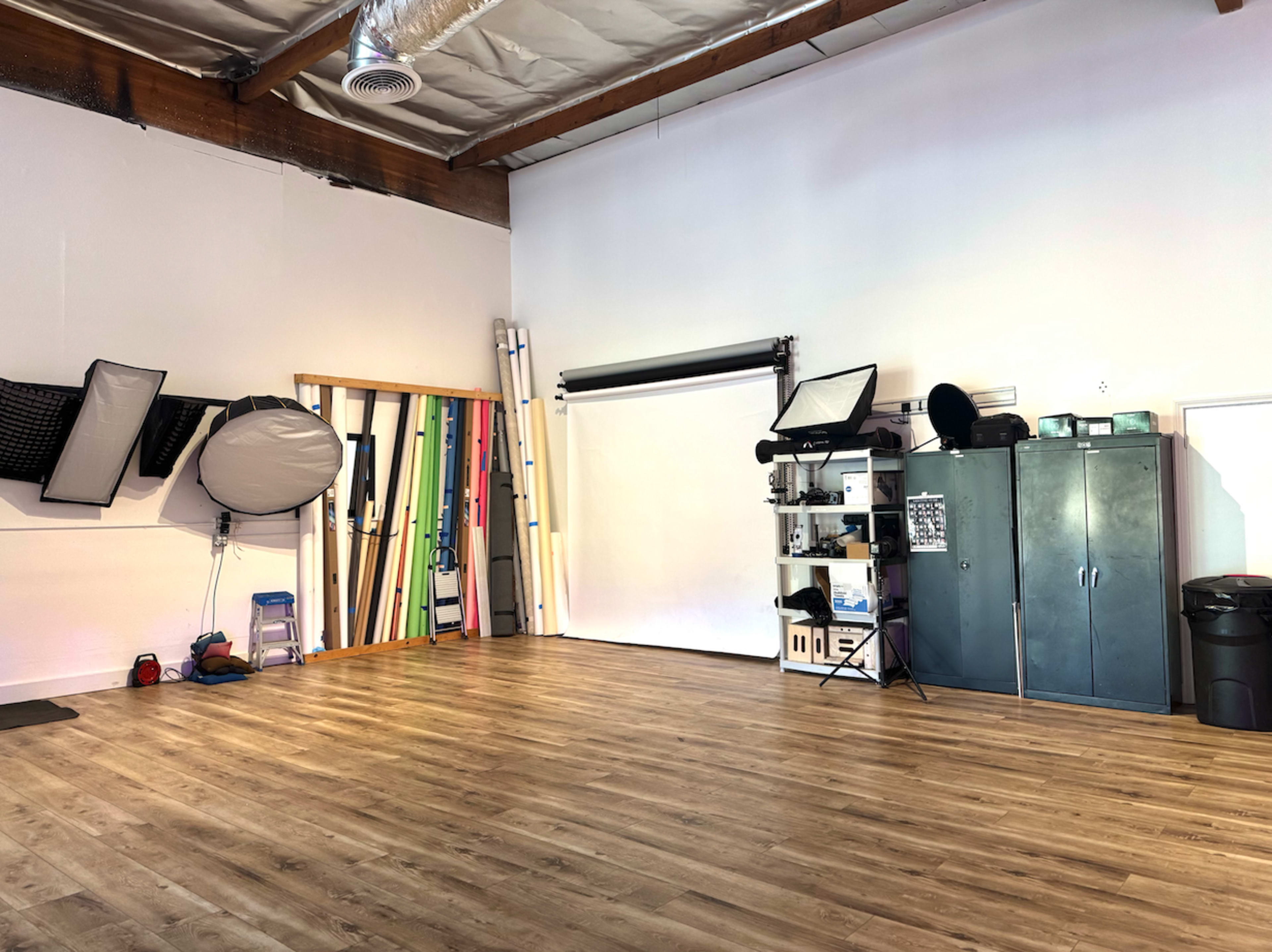 The image depicts a spacious photography studio with a white backdrop, various lighting equipment, and colorful backdrops mounted on the wall.