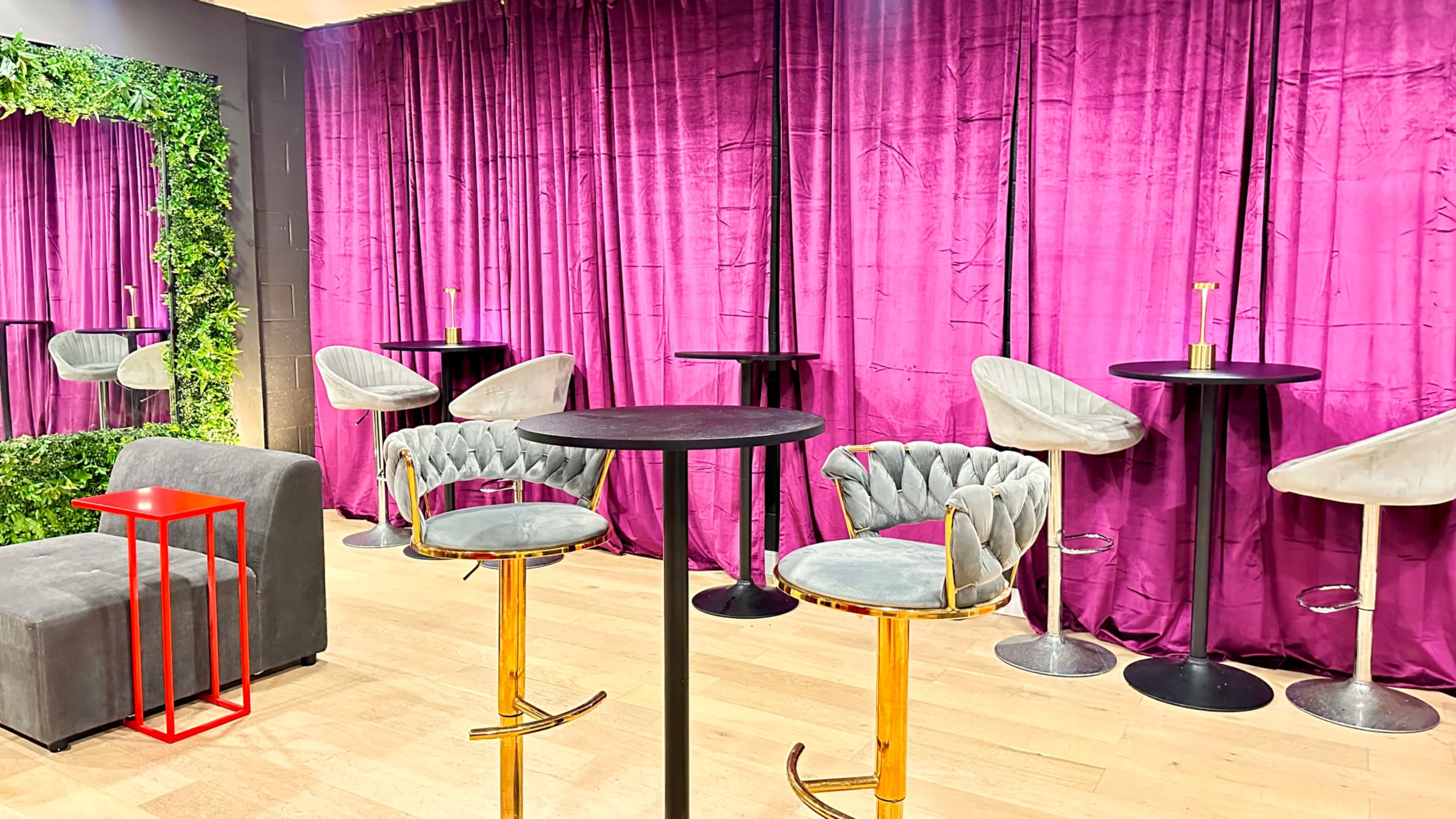The image shows a modern lounge area featuring purple drapes, a gray sofa, and several stylish round tables with high-backed chairs.