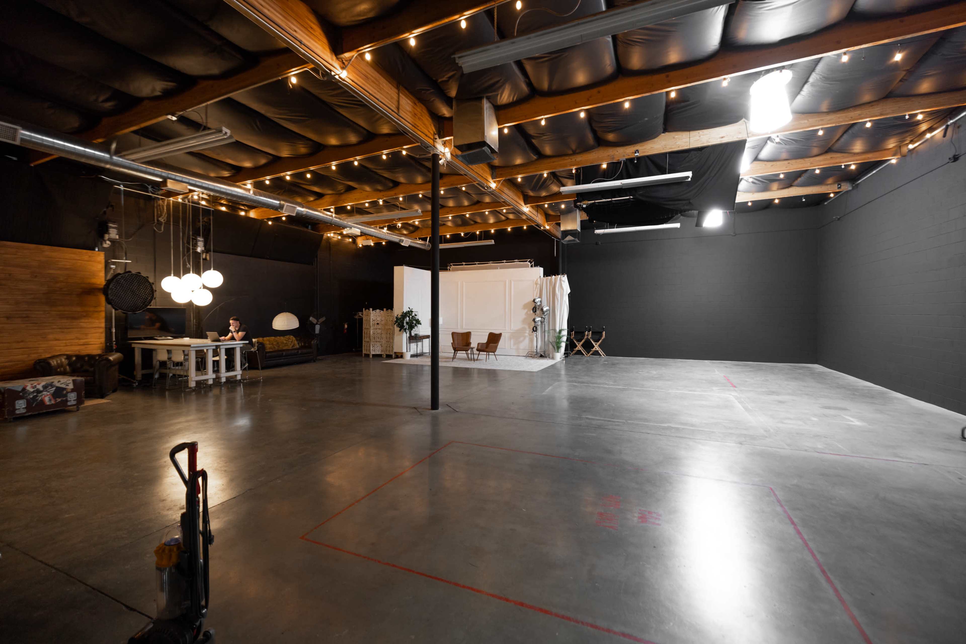 The image shows an expansive, industrial-style studio space with a polished concrete floor, wooden beams, and soft lighting.