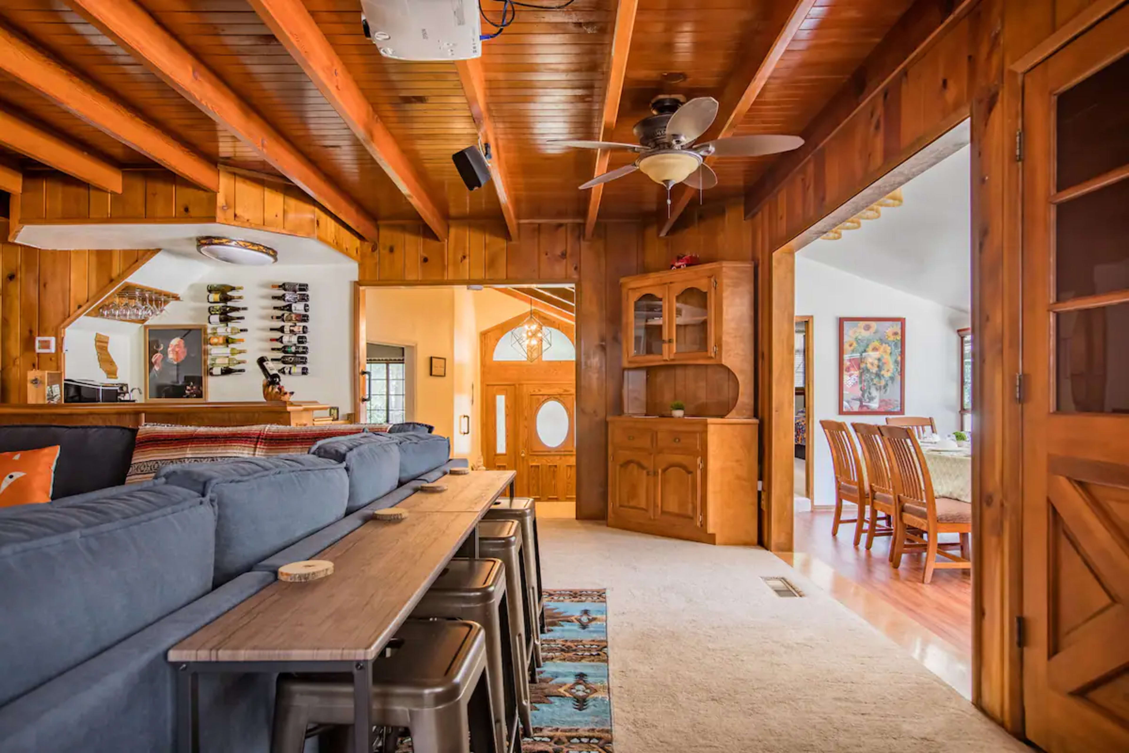 The image shows a wooden-paneled living room with a sofa, a dining area visible through an archway, and a console cabinet against the wall.