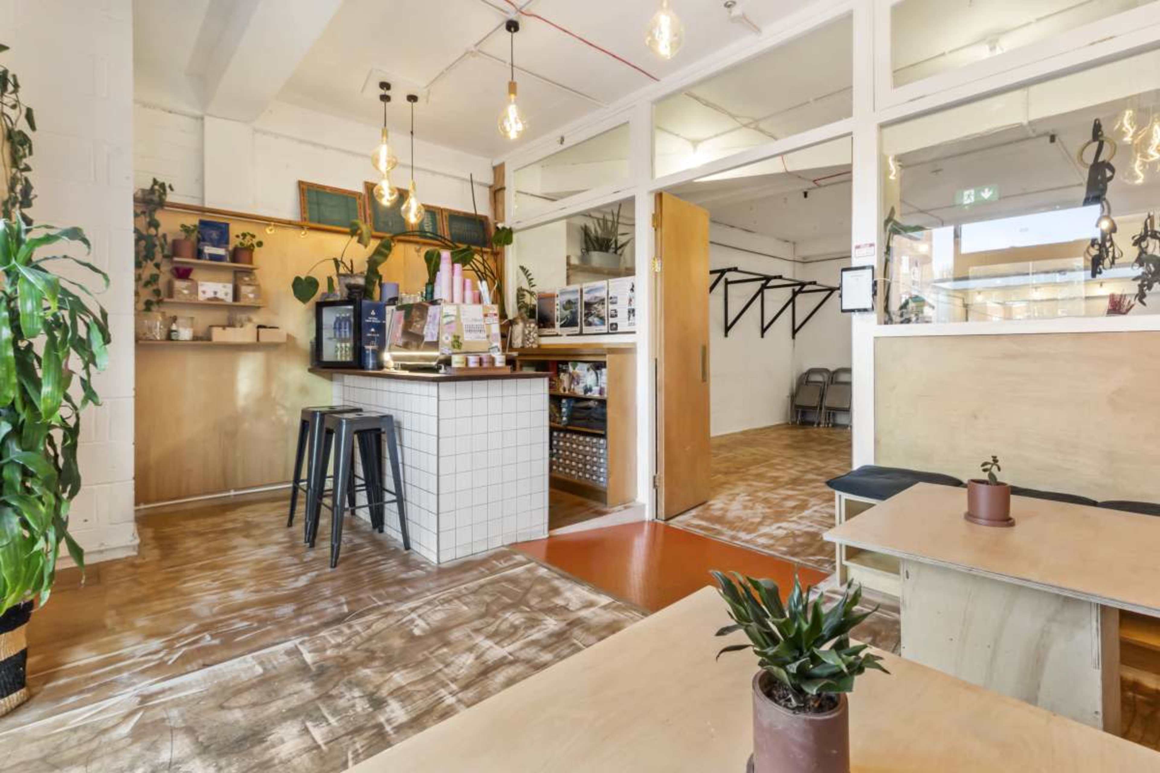 A modern cafe interior with a bar counter, wooden tables, and plants decorating the space.