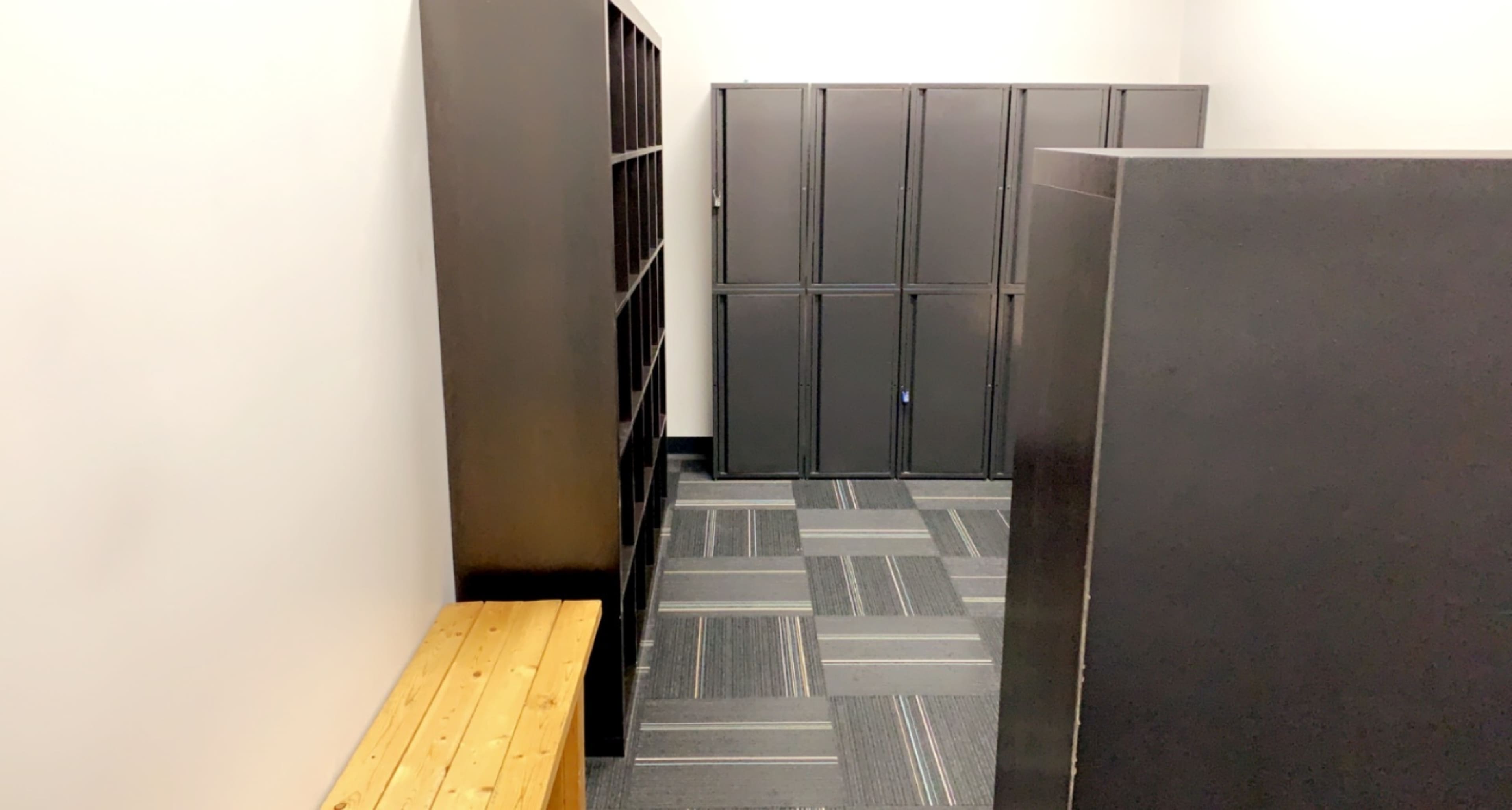 A small indoor space with a wooden bench, dark lockers, and shelving units along the walls.