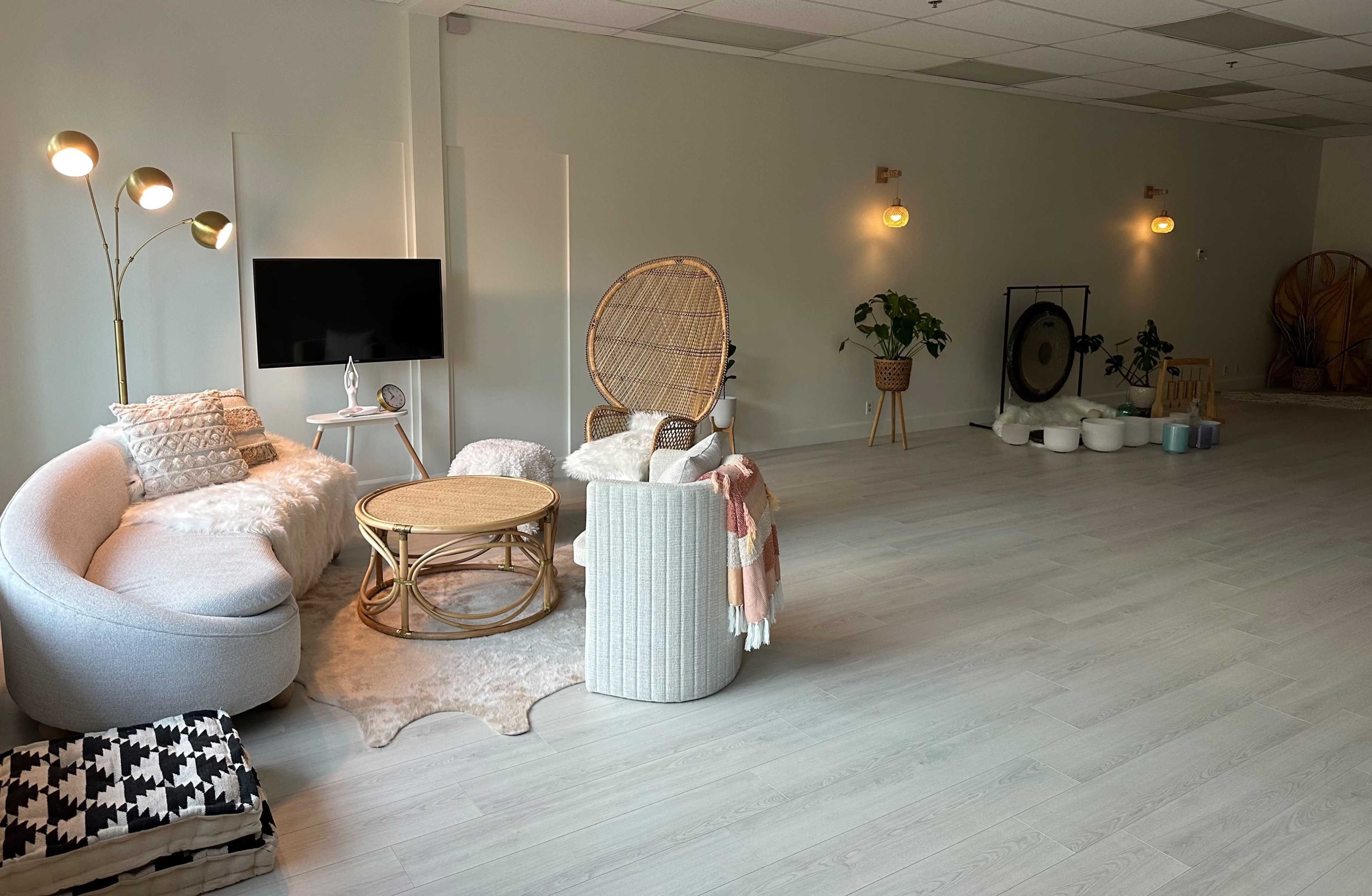 A spacious, softly lit room with comfortable seating, a television, and various plants, creating a relaxed atmosphere.