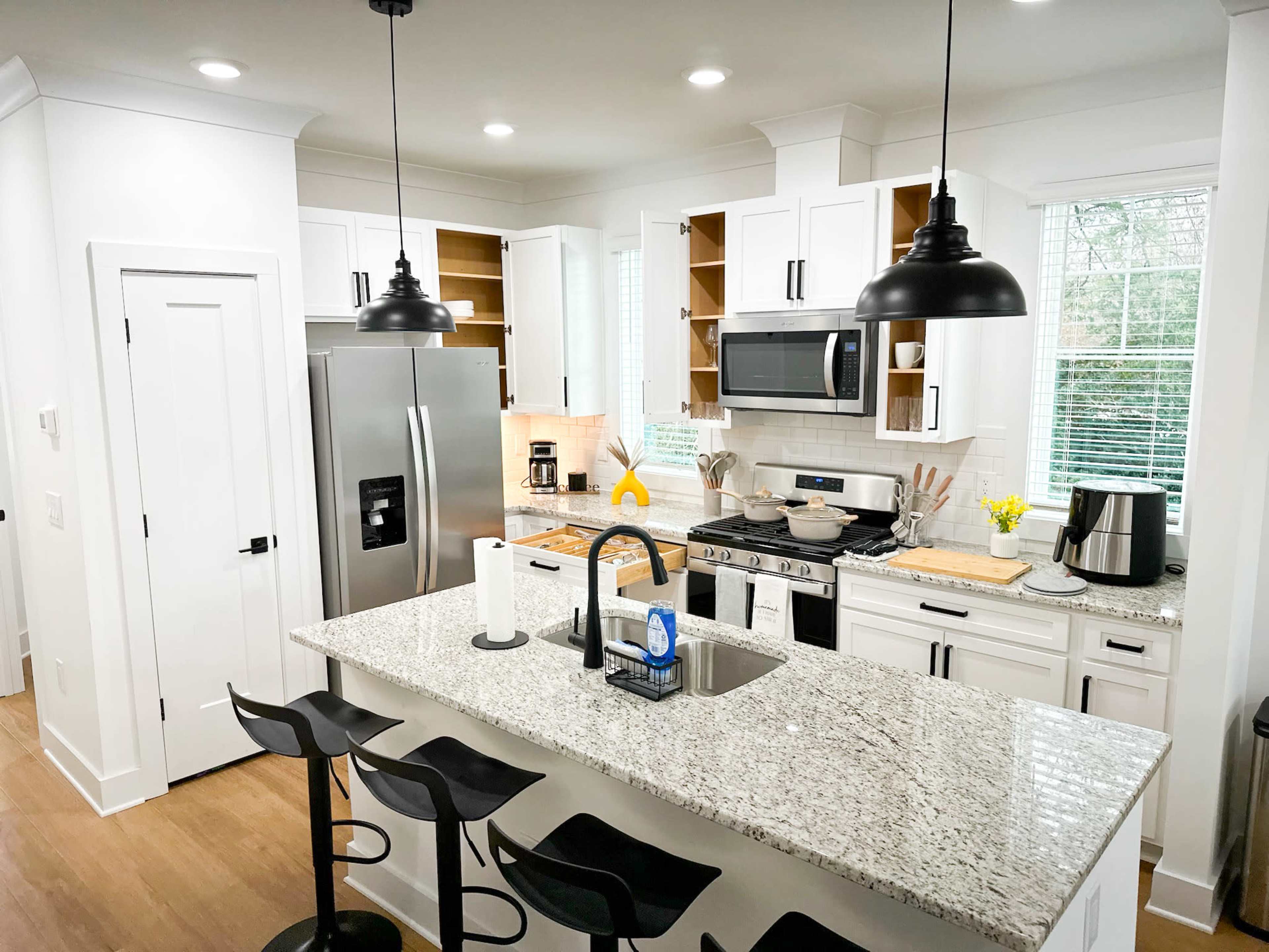 A modern kitchen features white cabinets, stainless steel appliances, and a large granite island with bar stools.