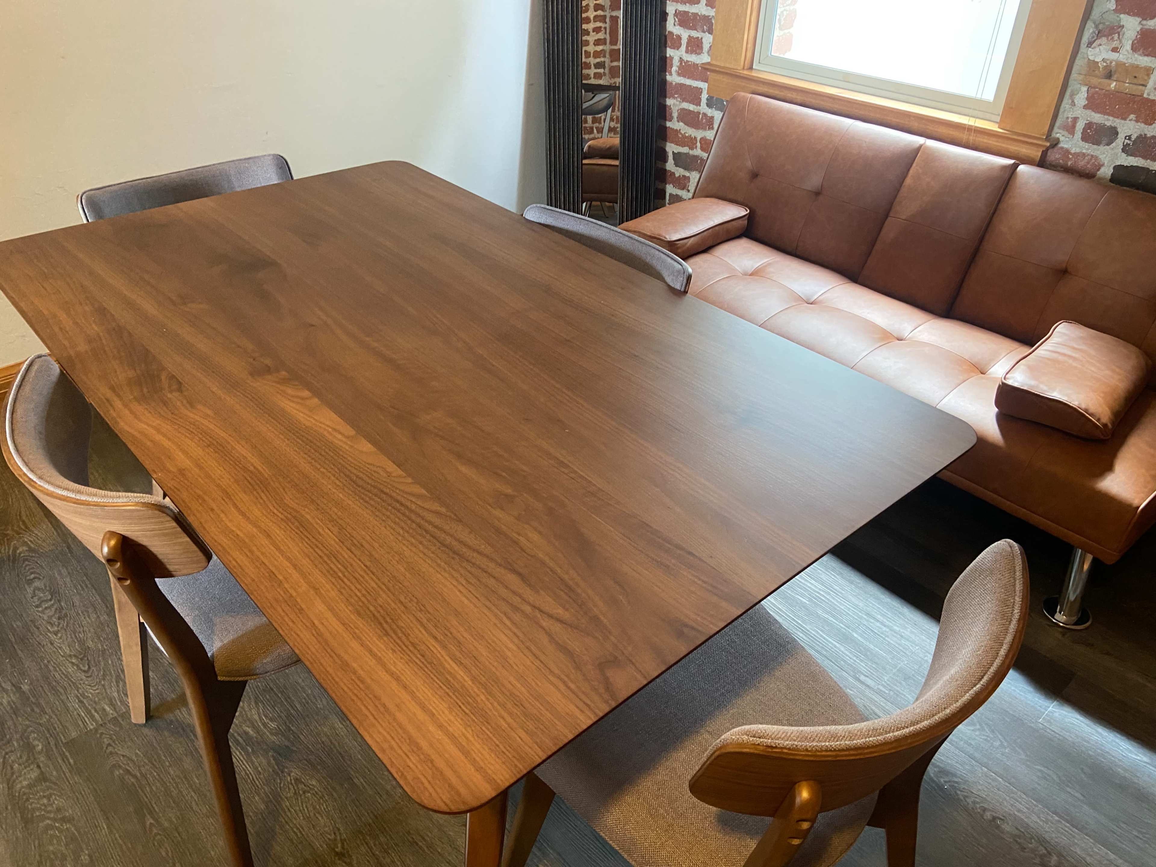 A wooden dining table sits in a room with a brown leather sofa and four chairs around it.