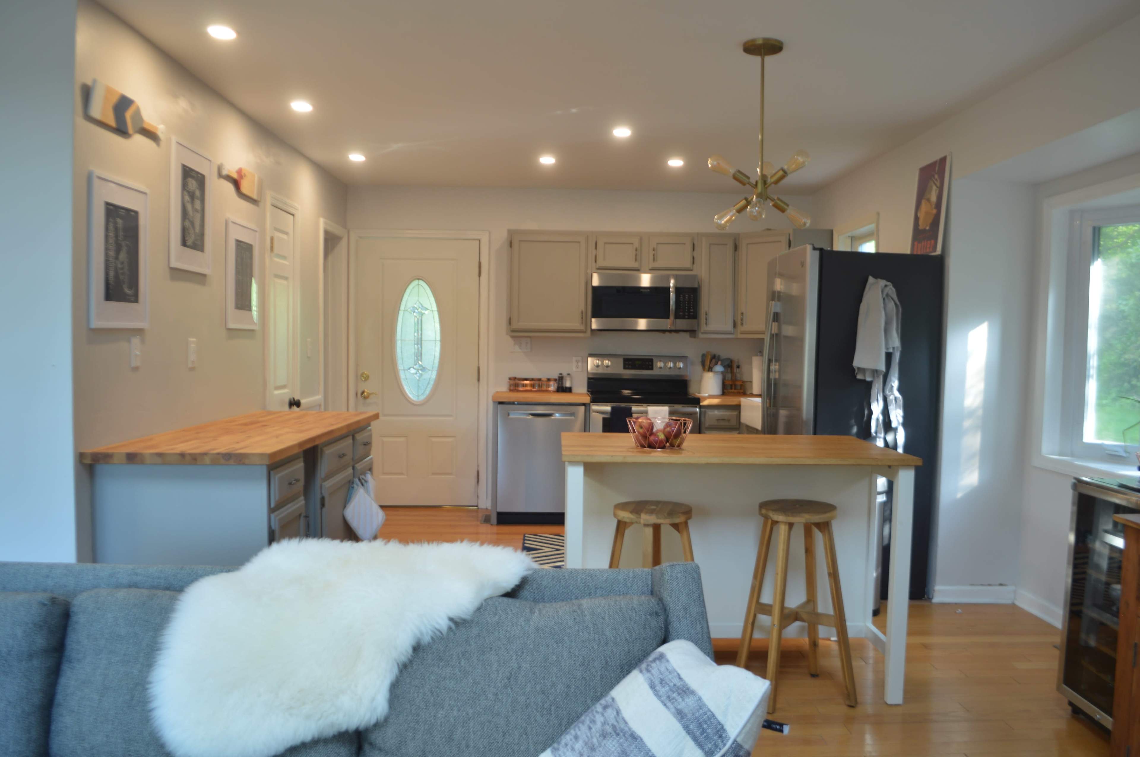 A modern kitchen and living area with light-colored cabinets, a wooden countertop island, and a cozy couch in the foreground.