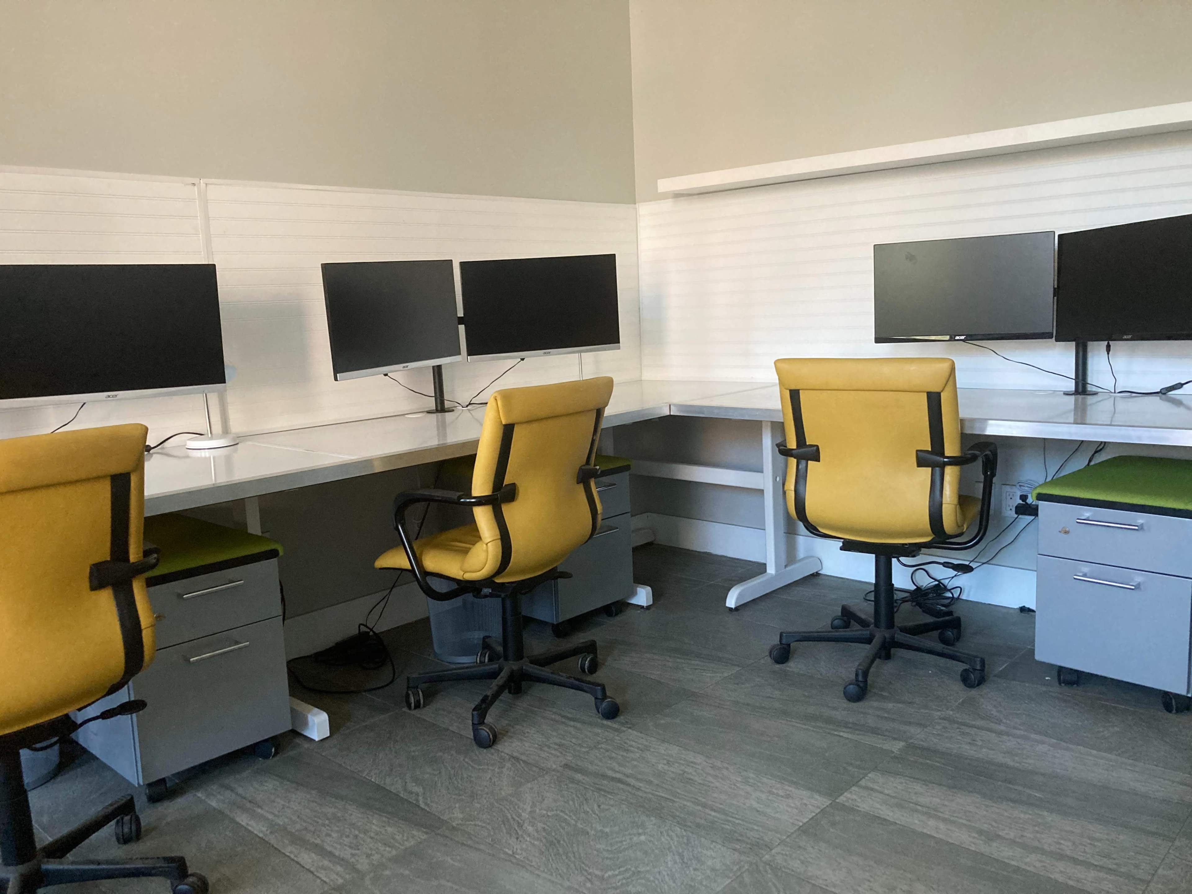 A workspace featuring two yellow office chairs and four computer monitors arranged on white desks.