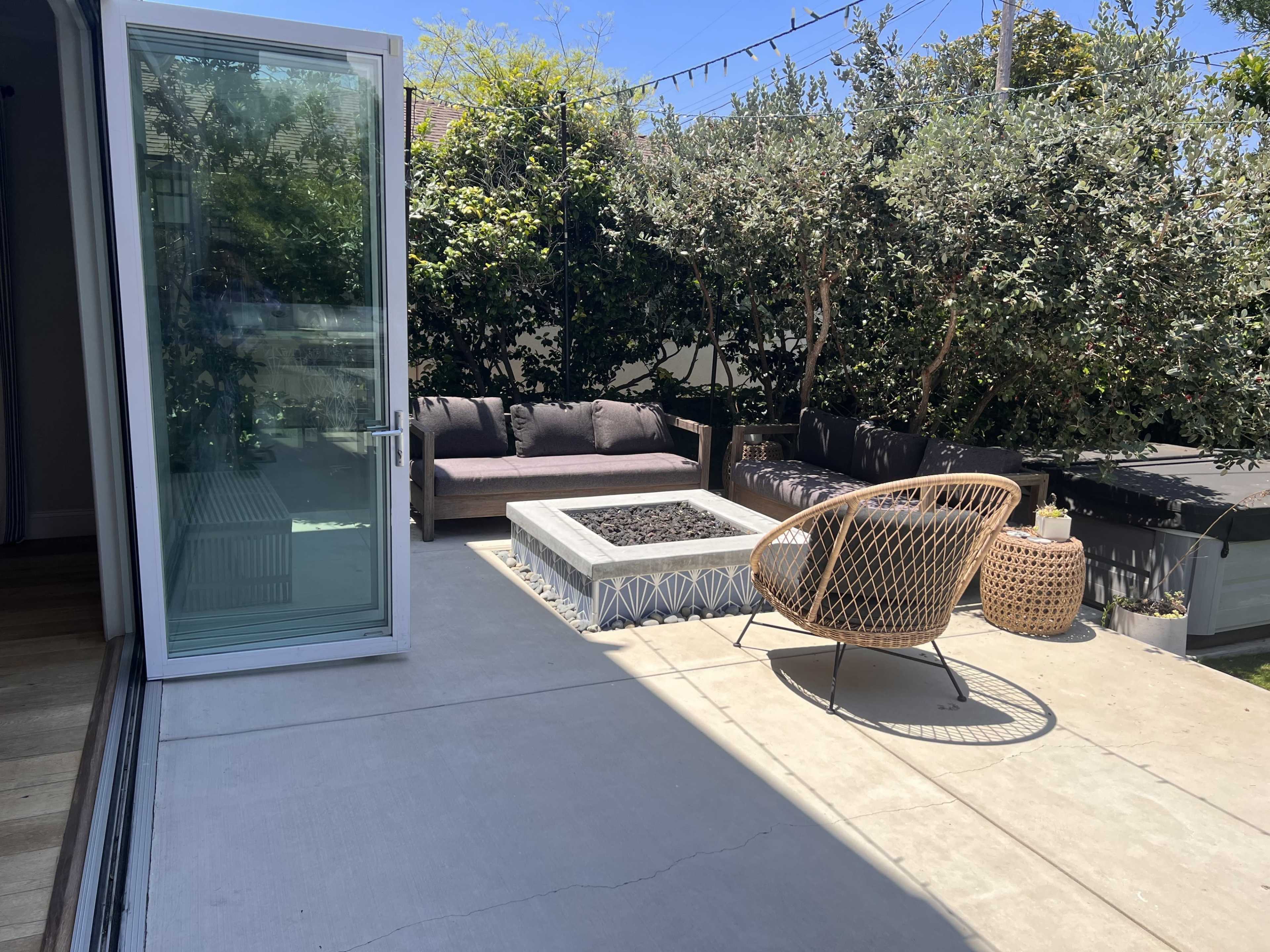 A patio features a modern fire pit surrounded by seating, with sliding glass doors leading into an interior space.