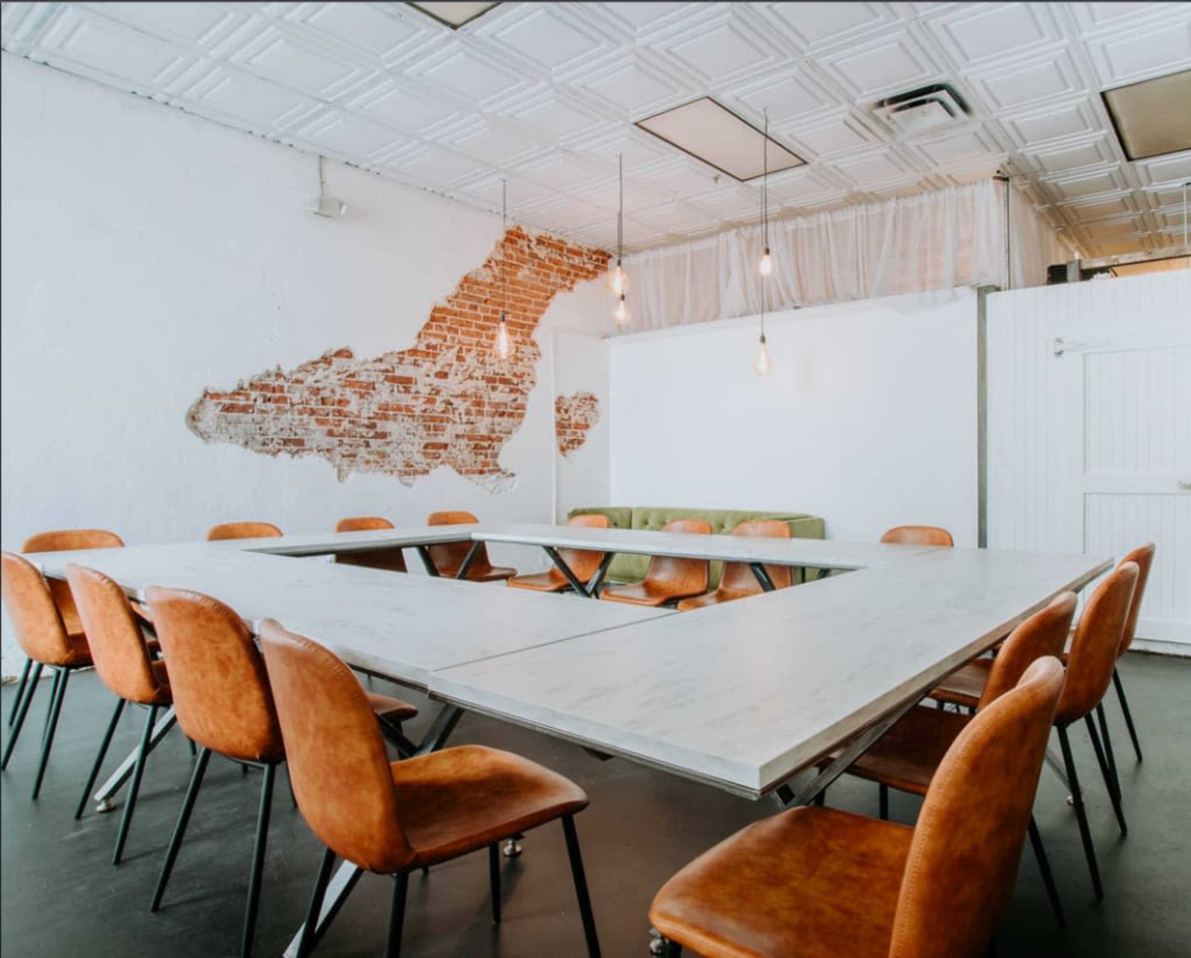 The image shows a meeting room with a large, rectangular table surrounded by brown chairs, and a wall featuring exposed red brick.