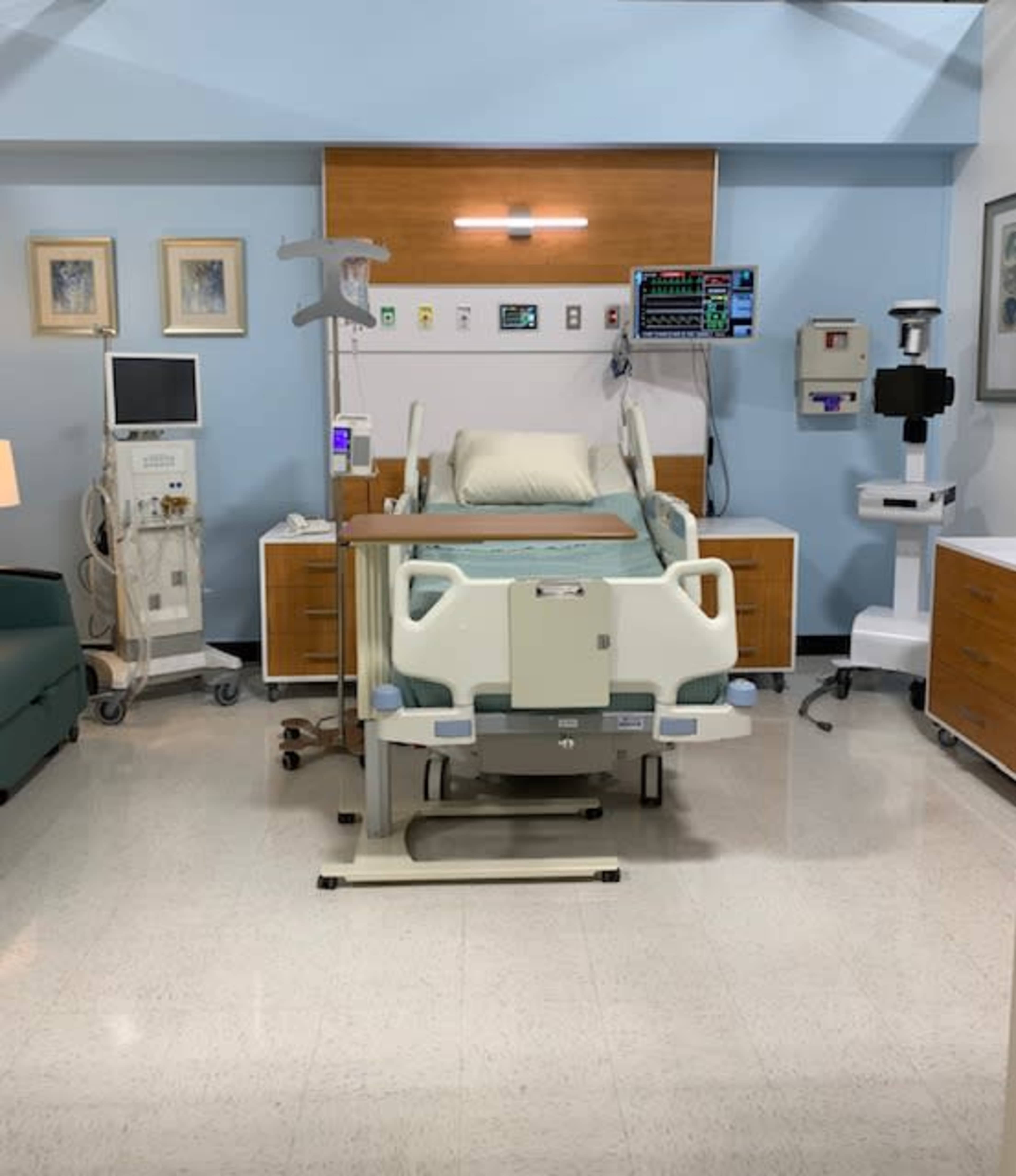 A hospital room with a bed, medical equipment, and furniture arranged in a clean, functional layout.