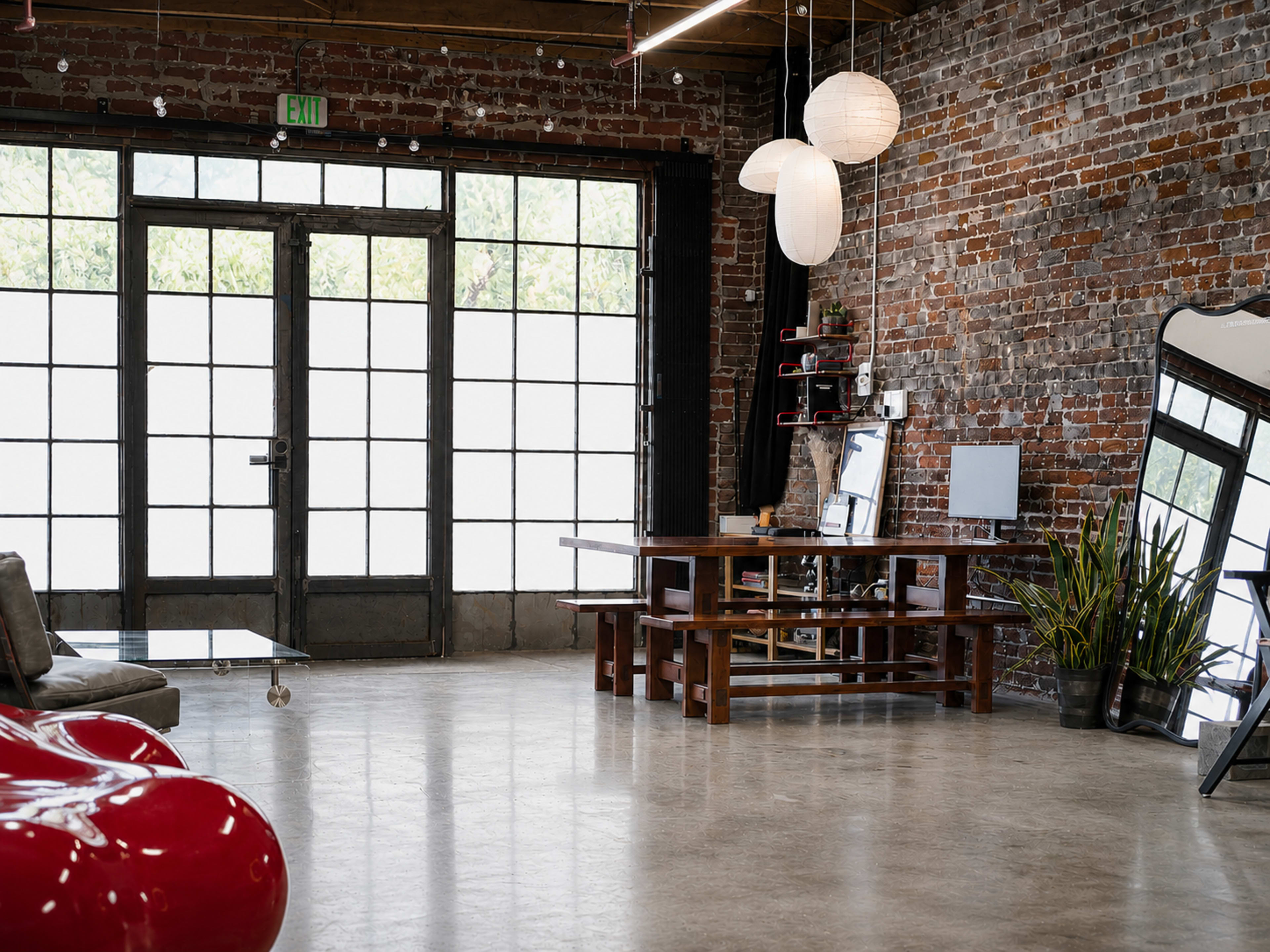 The interior space features exposed brick walls, large windows, a wooden table, and modern lighting fixtures.