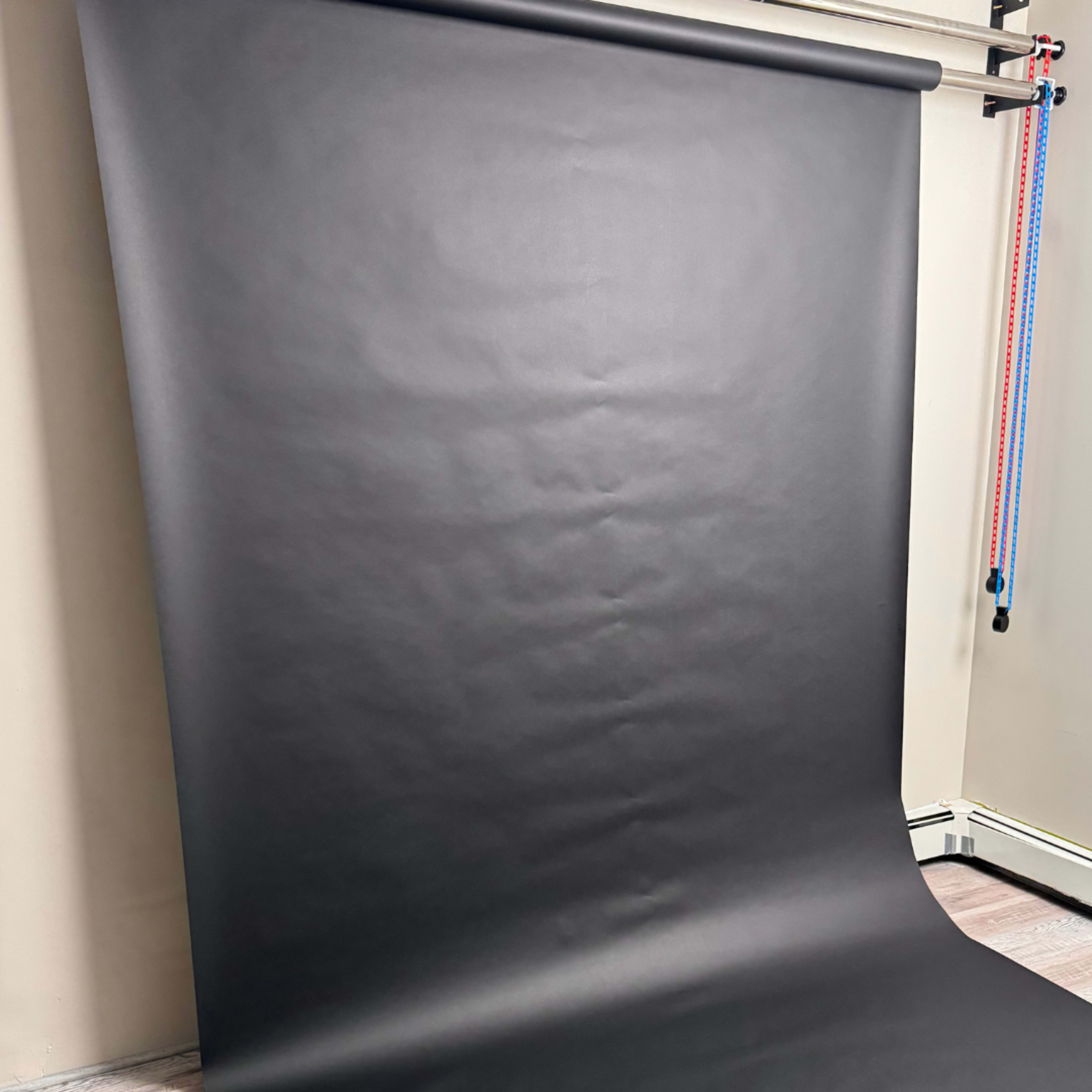 The image shows a large black backdrop set up against a wall, leaning slightly on a floor.