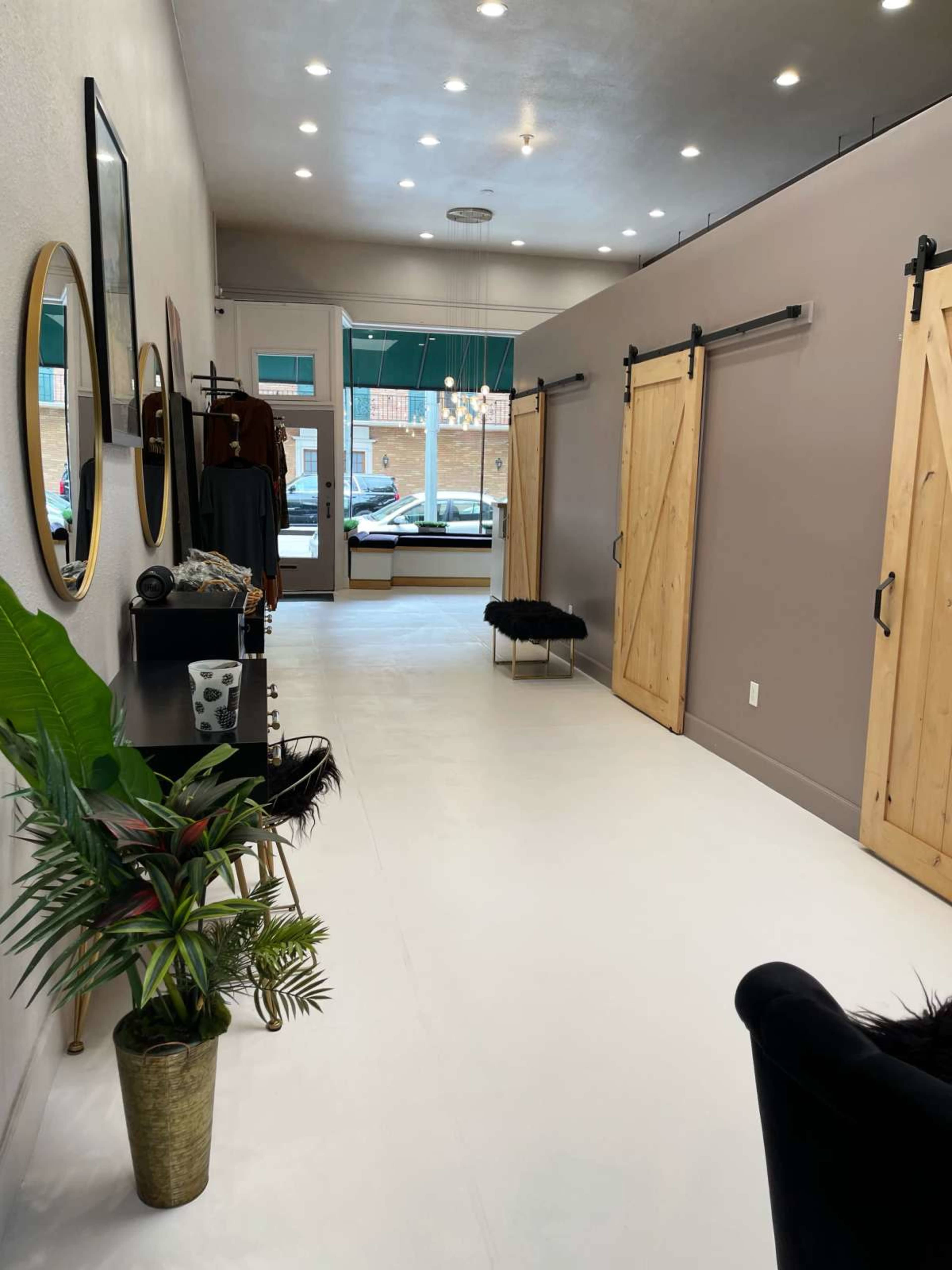 The image shows a spacious interior of a boutique with white flooring, wooden barn doors, and decorative elements including a plant and mirrors along the walls.