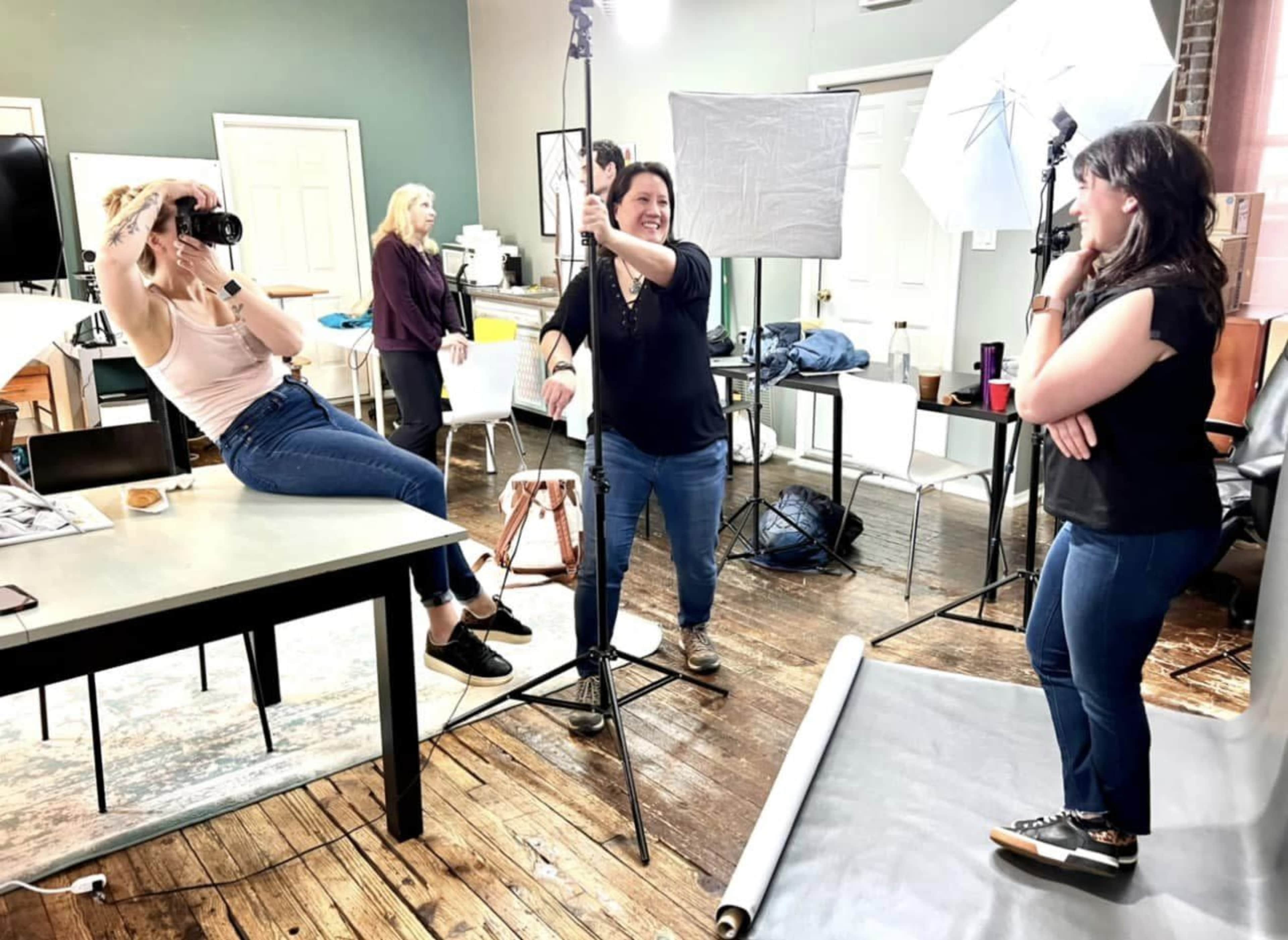 A group of photographers and their subject interact during a photo shoot in a studio setting.