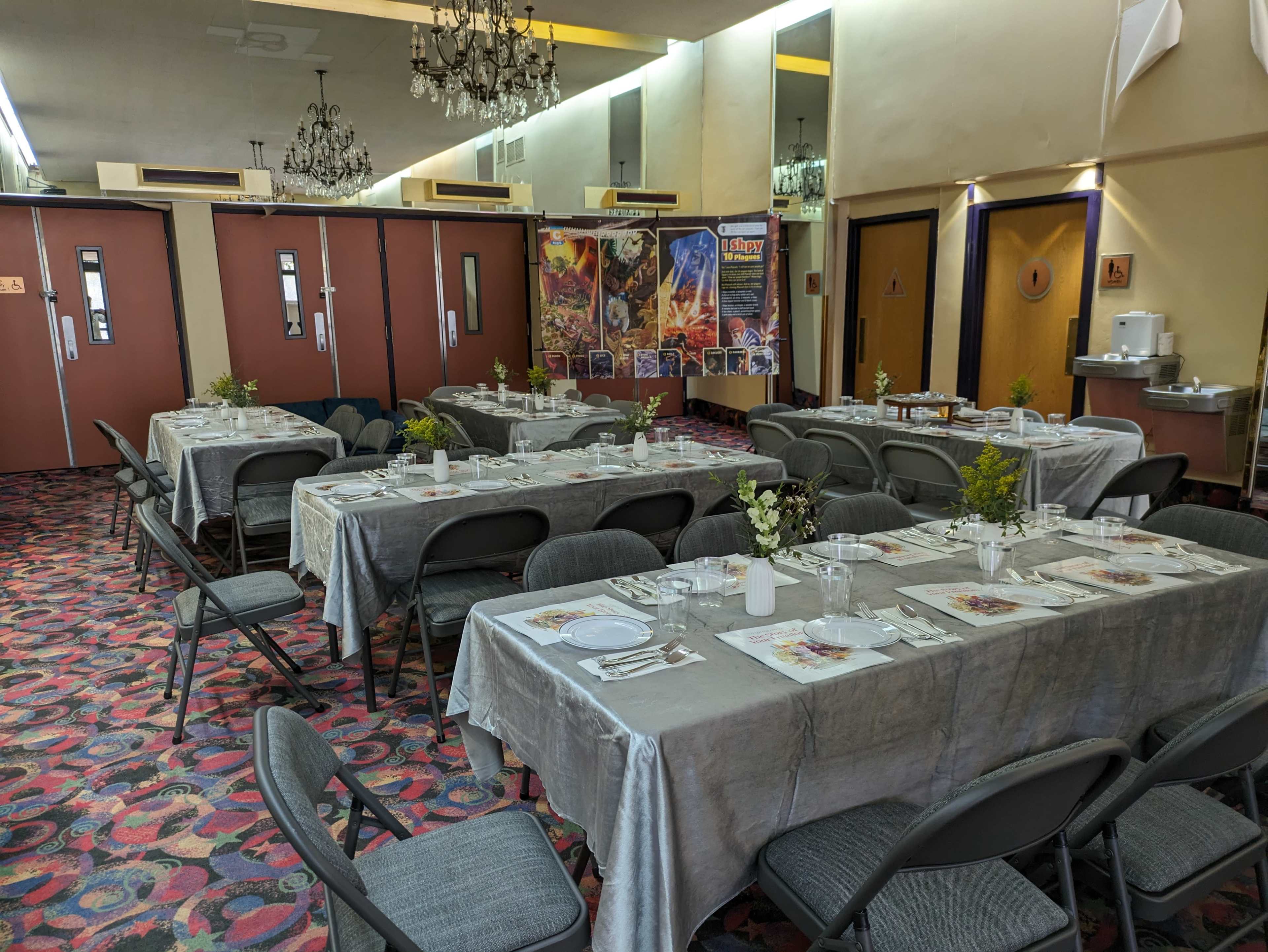 The image shows a banquet hall set up for an event with tables covered in gray tablecloths, arranged for dining, and decorated with floral centerpieces.
