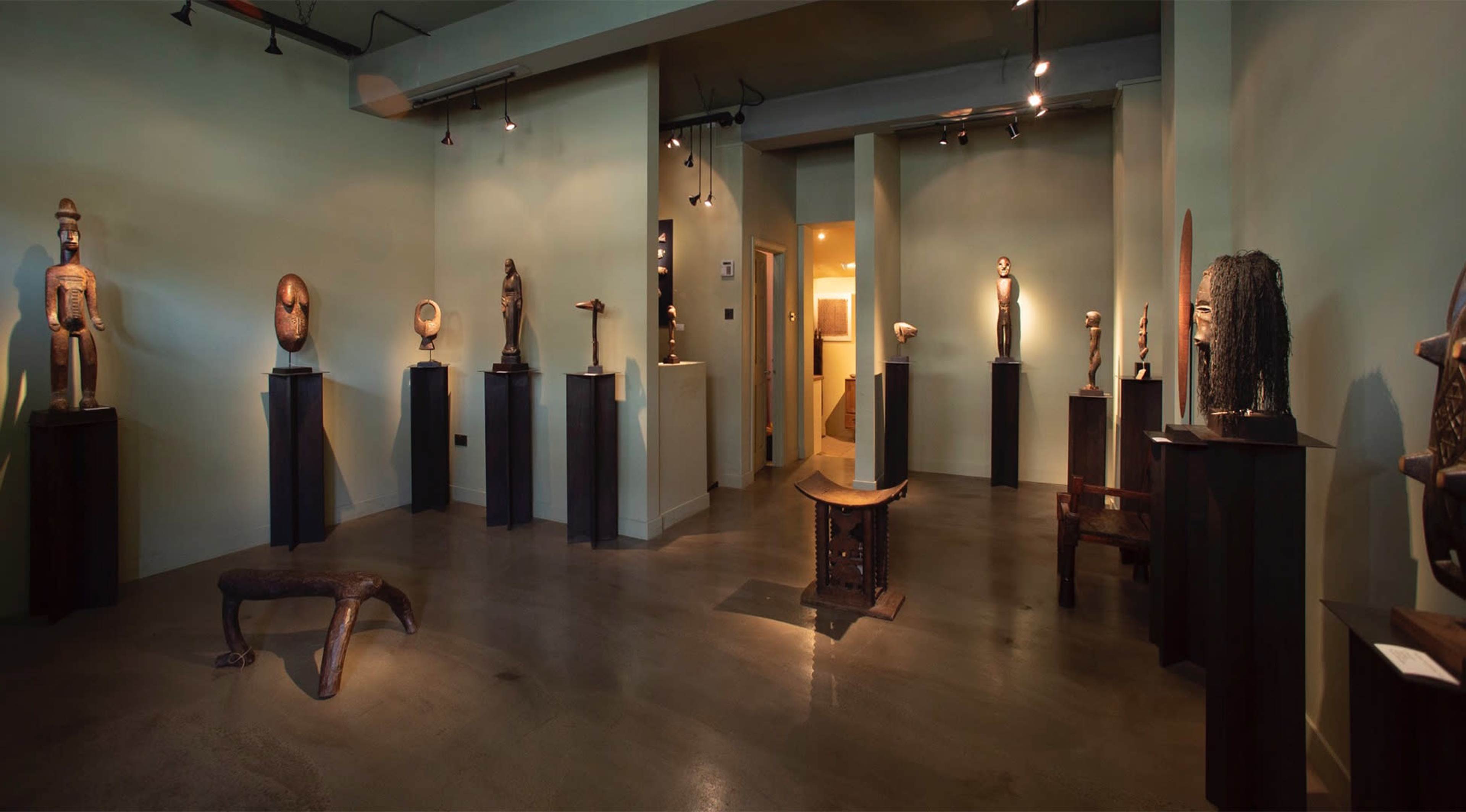 An art gallery featuring a variety of sculptures displayed on pedestals within a green-walled space.