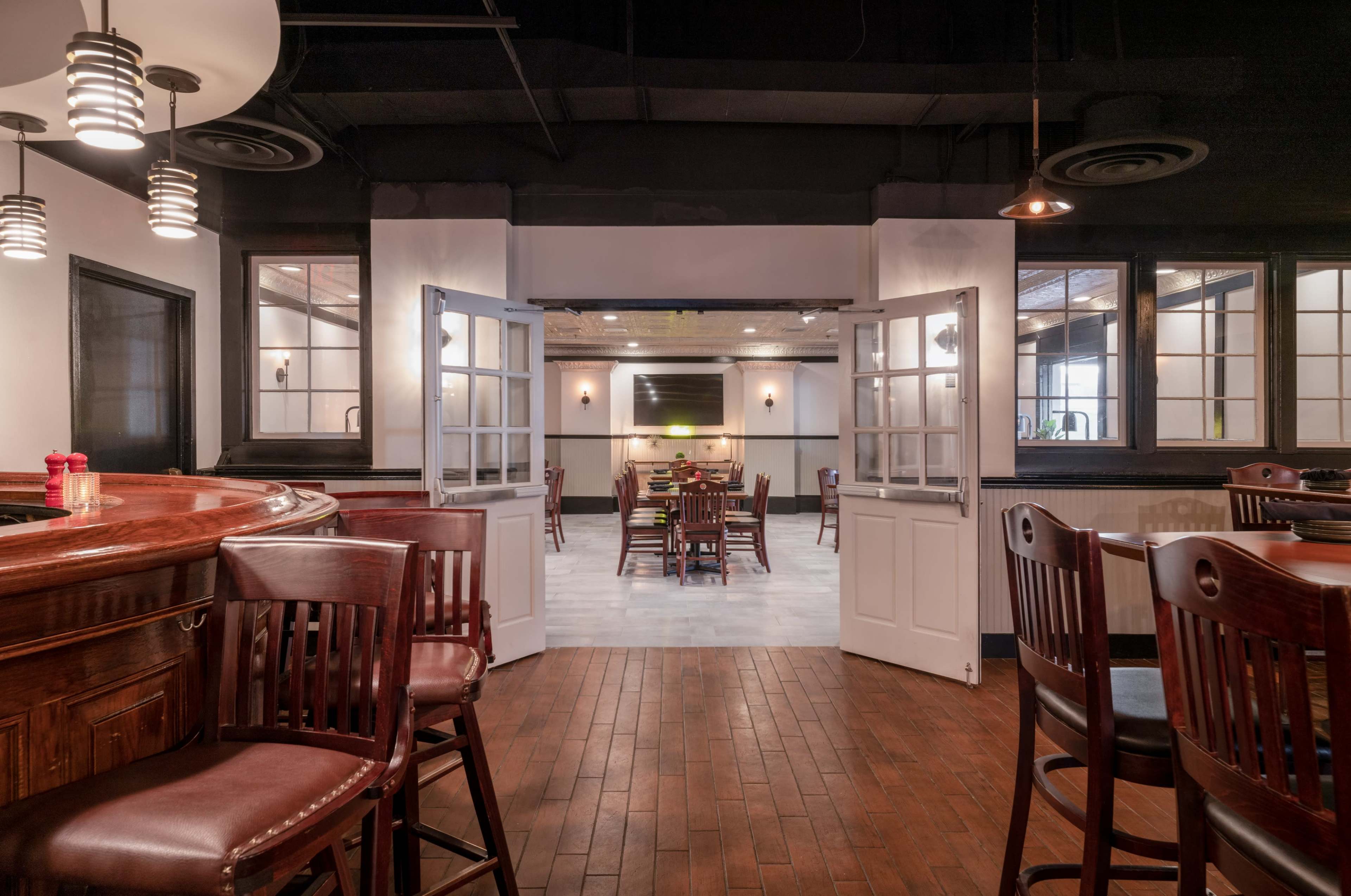 A restaurant interior with a bar area in the foreground and an open dining space visible through double doors in the background.