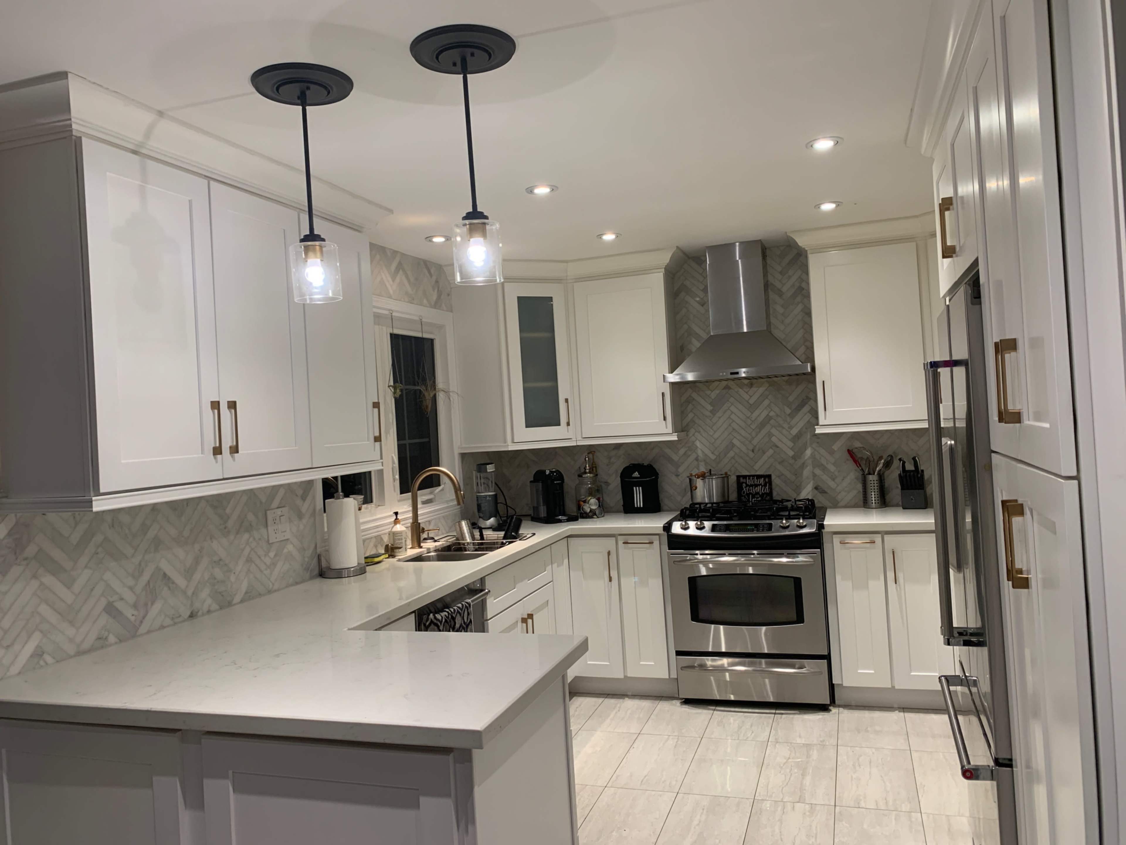 A modern kitchen features white cabinetry, a gray chevron backsplash, stainless steel appliances, and pendant lighting.